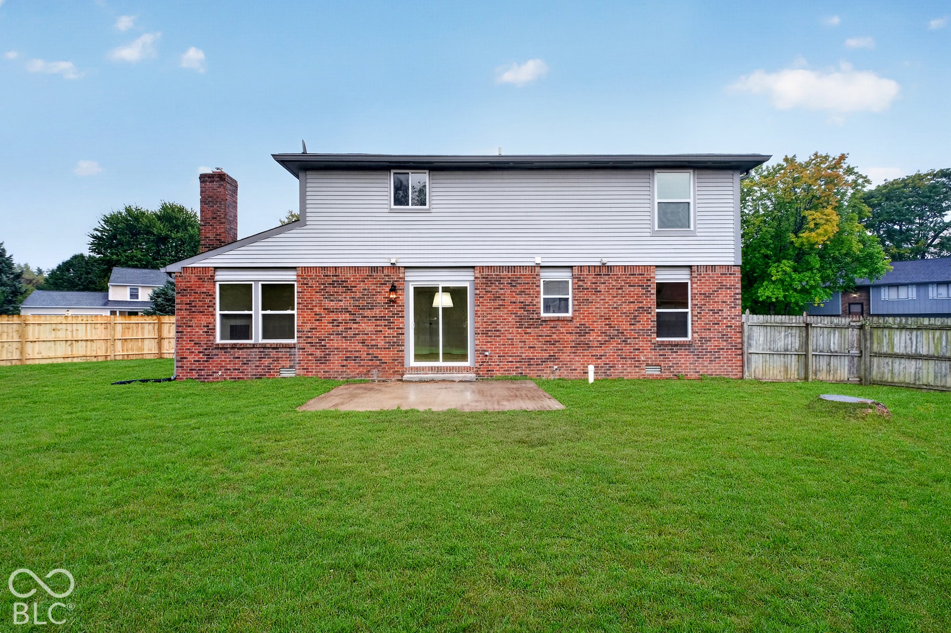 Rear exterior featuring a brick and vinyl siding facade, a concrete patio, a brick chimney, and a fenced-in grass backyard