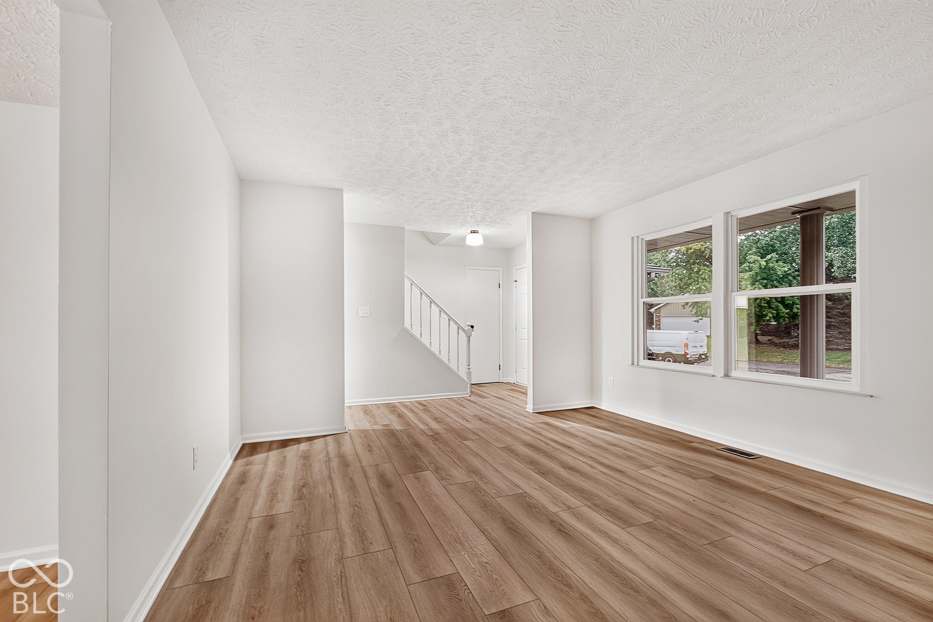 Interior space featuring wood-finish flooring, dual windows, and a staircase with a white balustrade