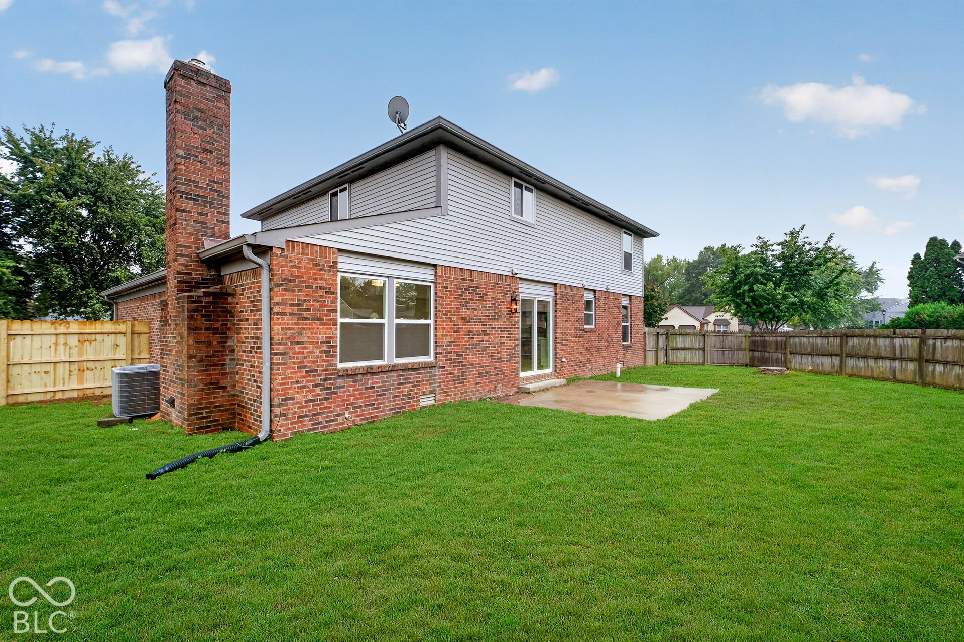 Rear exterior featuring a brick and vinyl siding facade, an exterior brick chimney, a concrete patio, and a fully fenced backyard