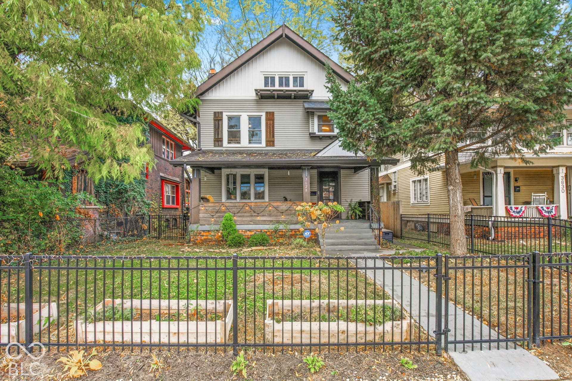 Two-story exterior featuring lap siding, gabled roofline, covered front porch, decorative wood shutters, and metal perimeter fencing