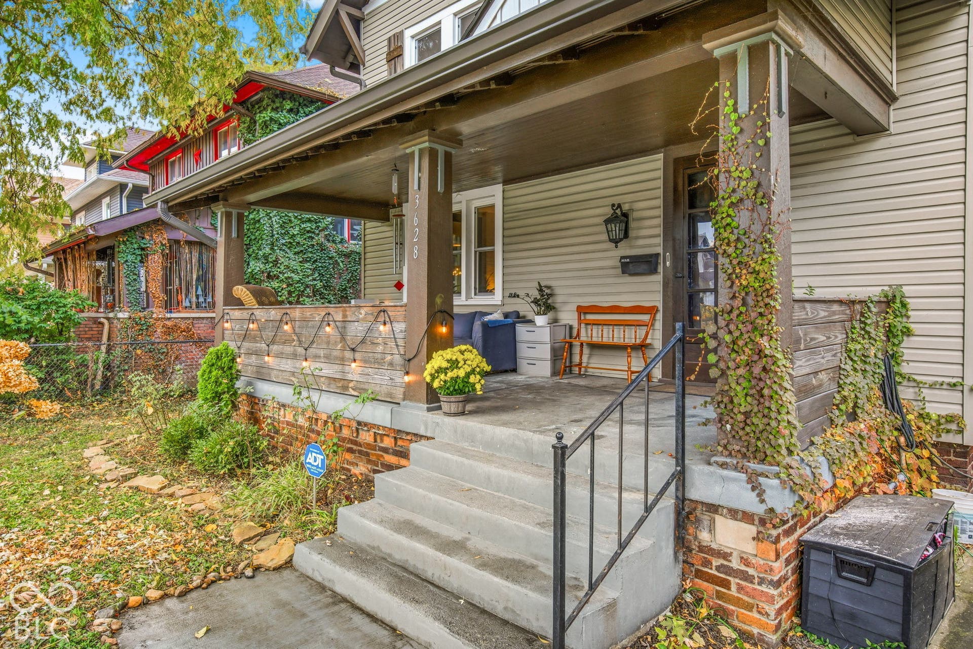 Covered front porch featuring wood-panel siding, concrete steps with wrought iron railing, and brick foundation detailing
