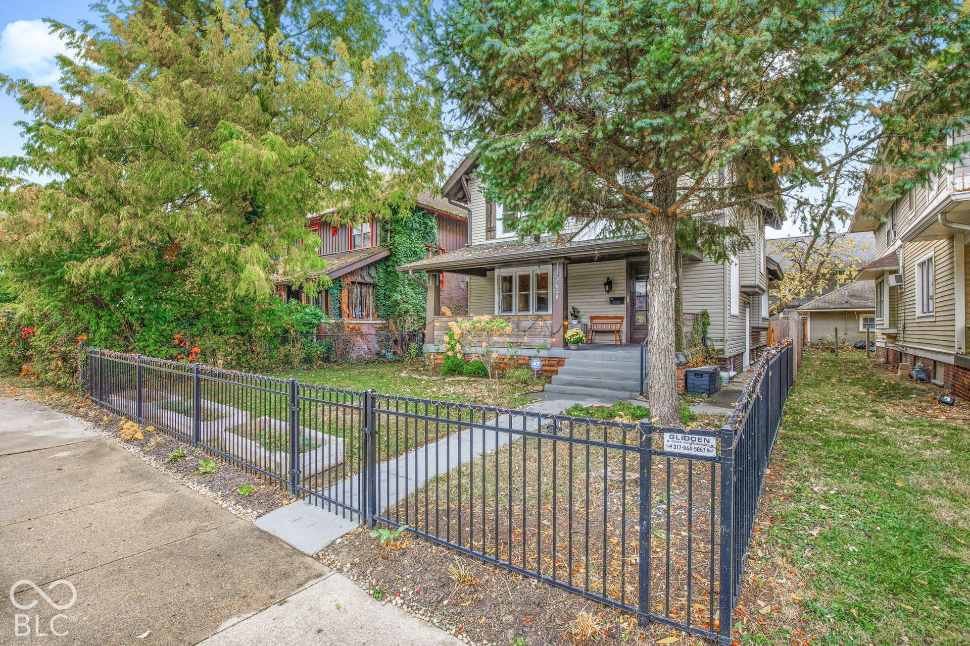 Two-story residence featuring horizontal lap siding, an expansive covered front porch, concrete steps, and a decorative metal perimeter fence