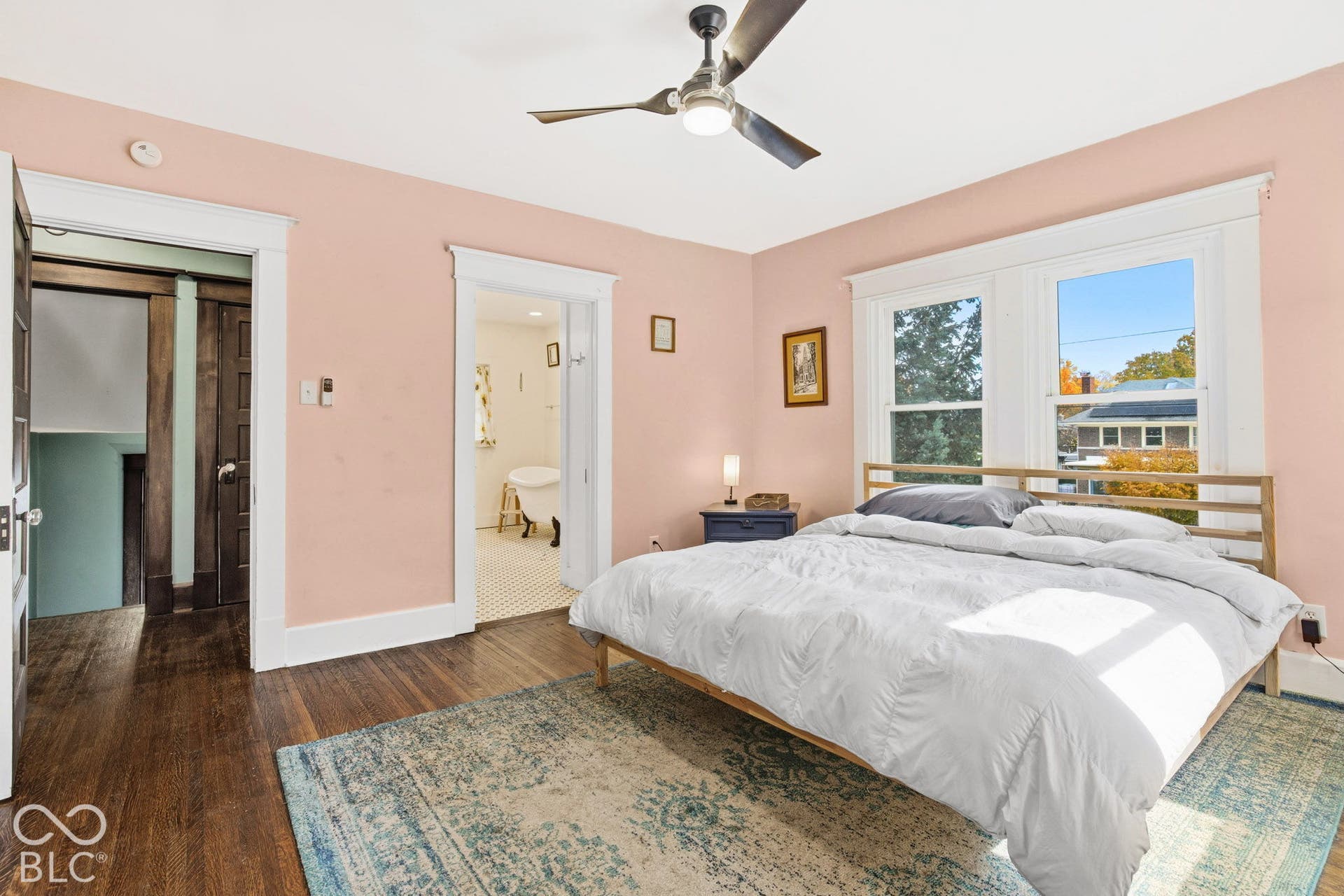 Wood-finish flooring, double-hung windows with white casing, and a brushed nickel ceiling fan with integrated lighting