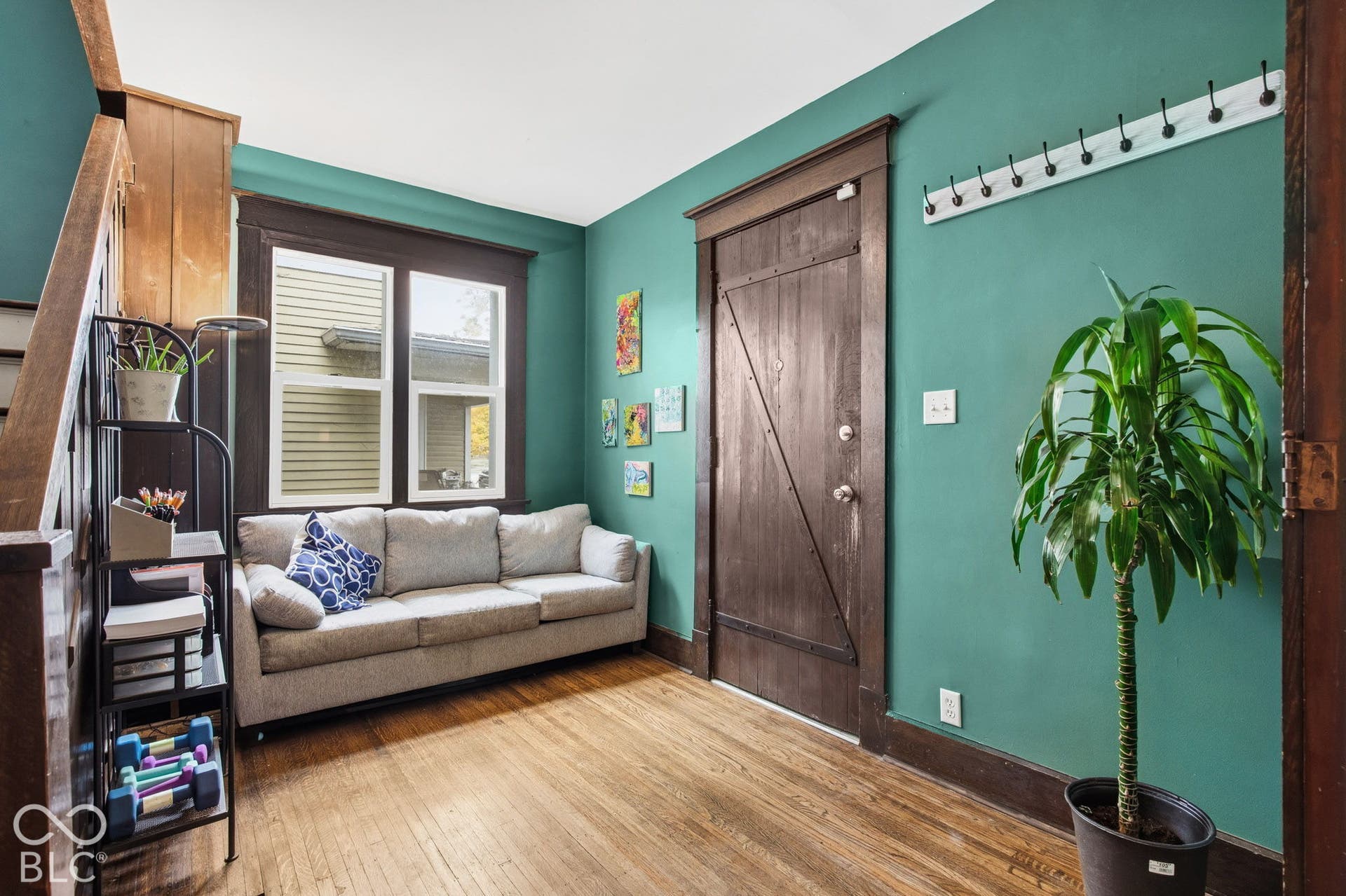 Hardwood flooring, natural wood-finish door with diagonal bracing, stained wood window casing, and wall-mounted coat rack