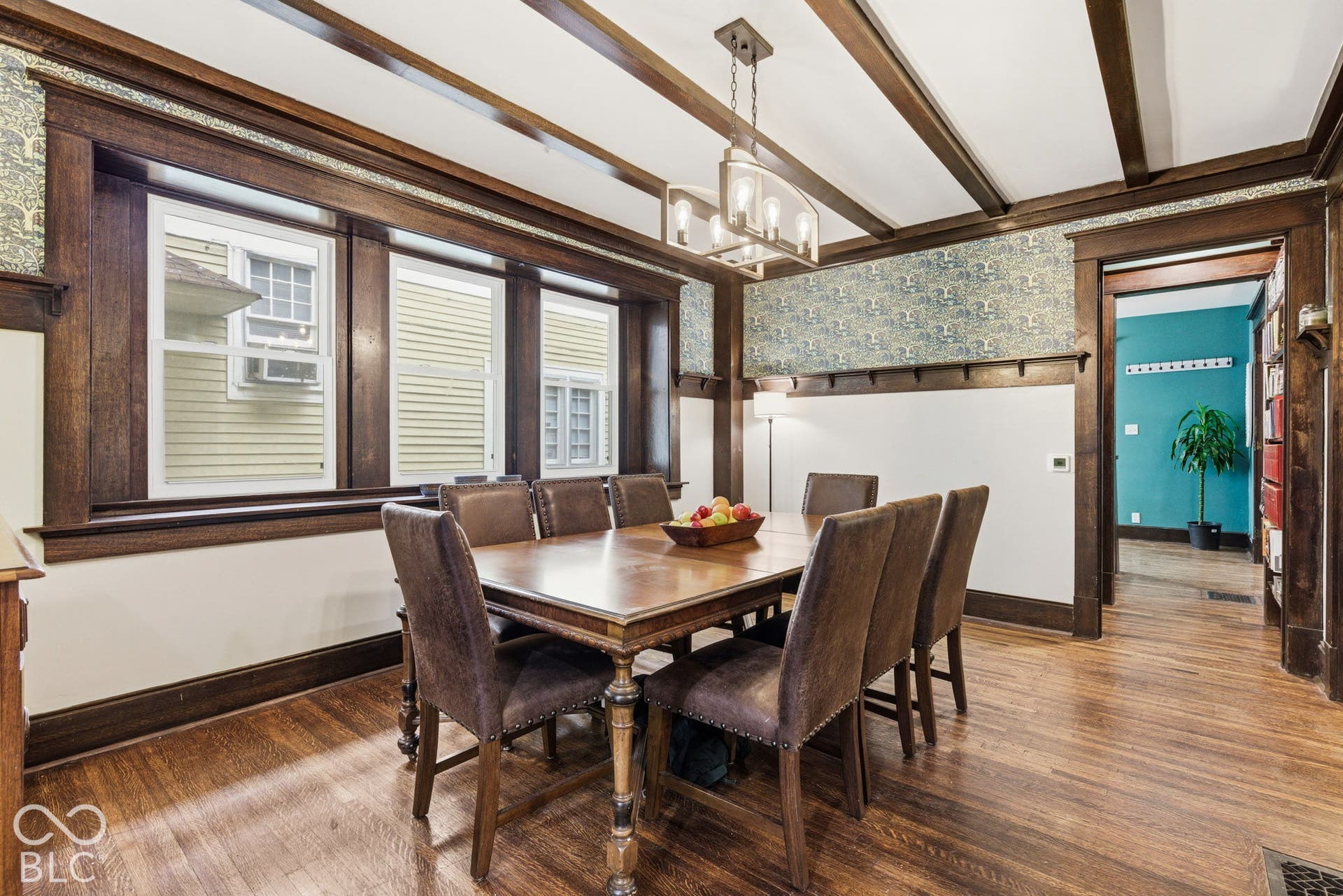 Dark stained wood trim and exposed ceiling beams, wood-finish flooring, built-in plate rail, and multi-light chandelier