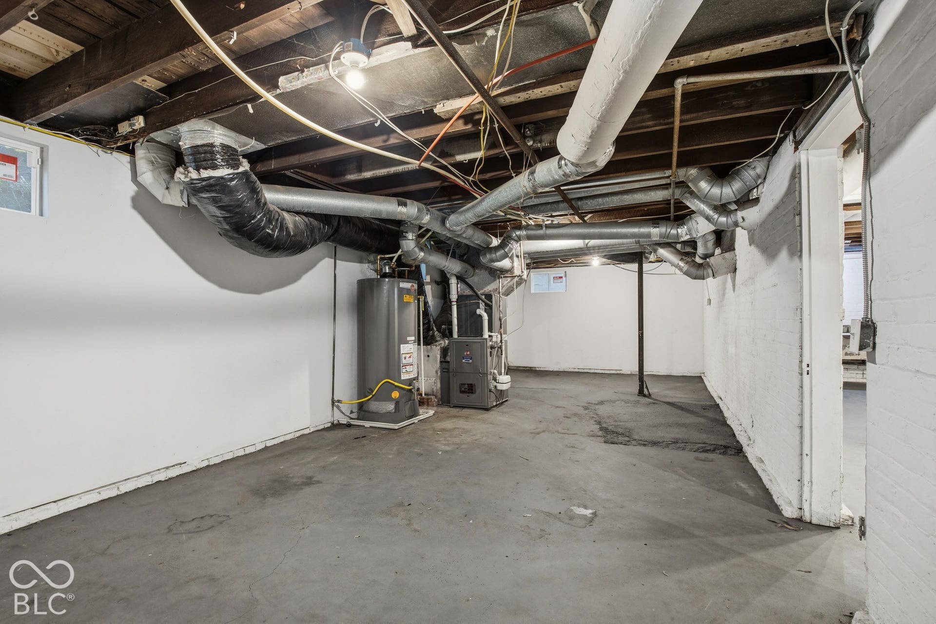 Unfinished storage space with concrete flooring, painted masonry walls, exposed ceiling joists, and mechanical systems including a water heater and furnace