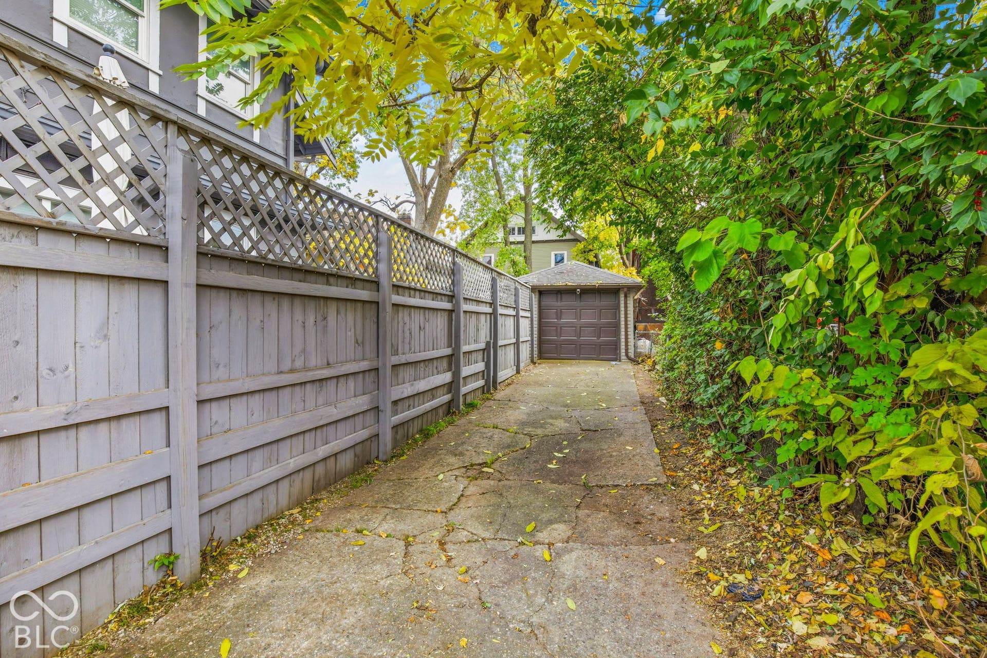 Concrete driveway featuring a detached garage, privacy fencing with lattice detail, and mature perimeter landscaping