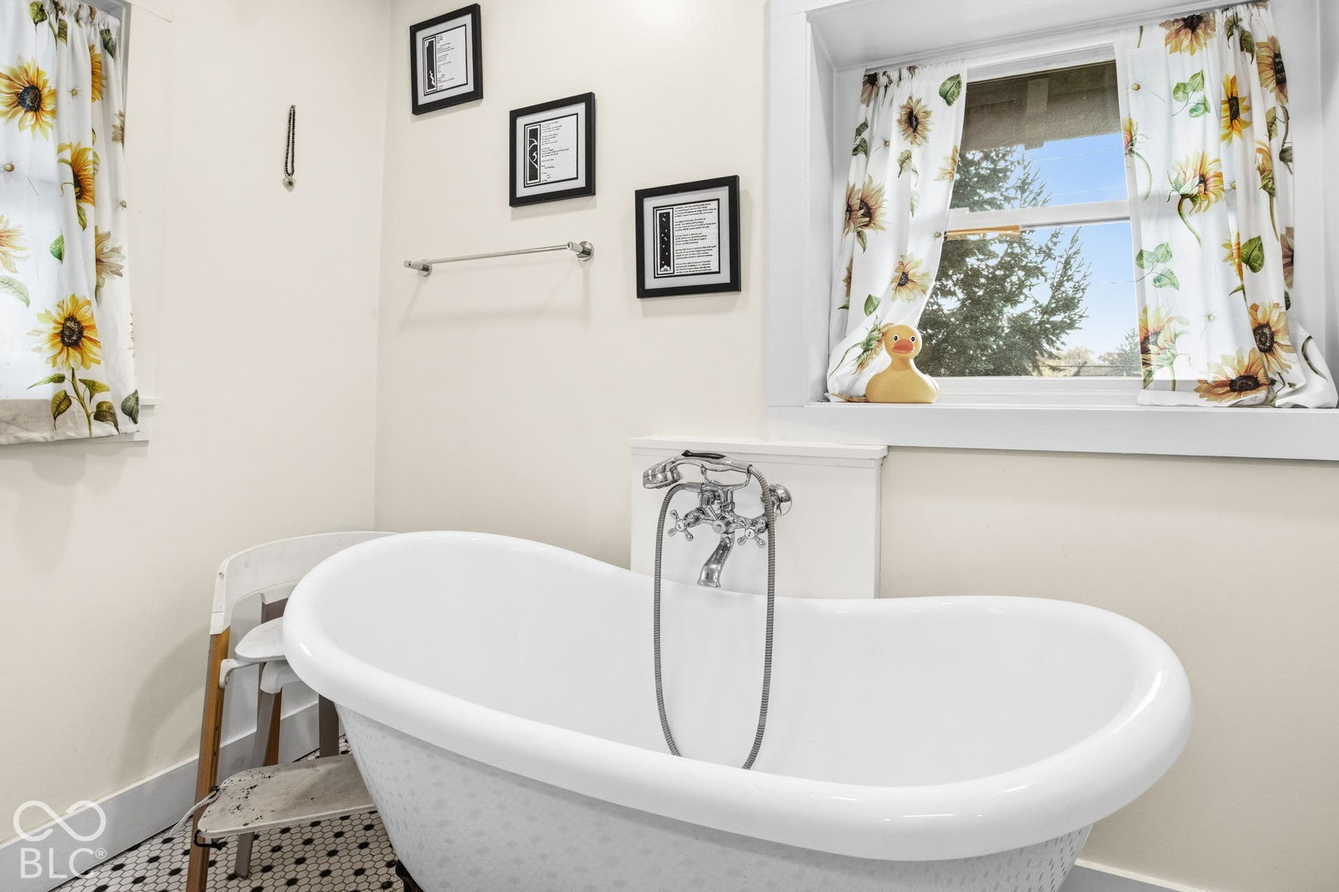 Freestanding soaking tub with a chrome telephone-style faucet, set against a backdrop of double-hung windows and black-and-white penny tile flooring