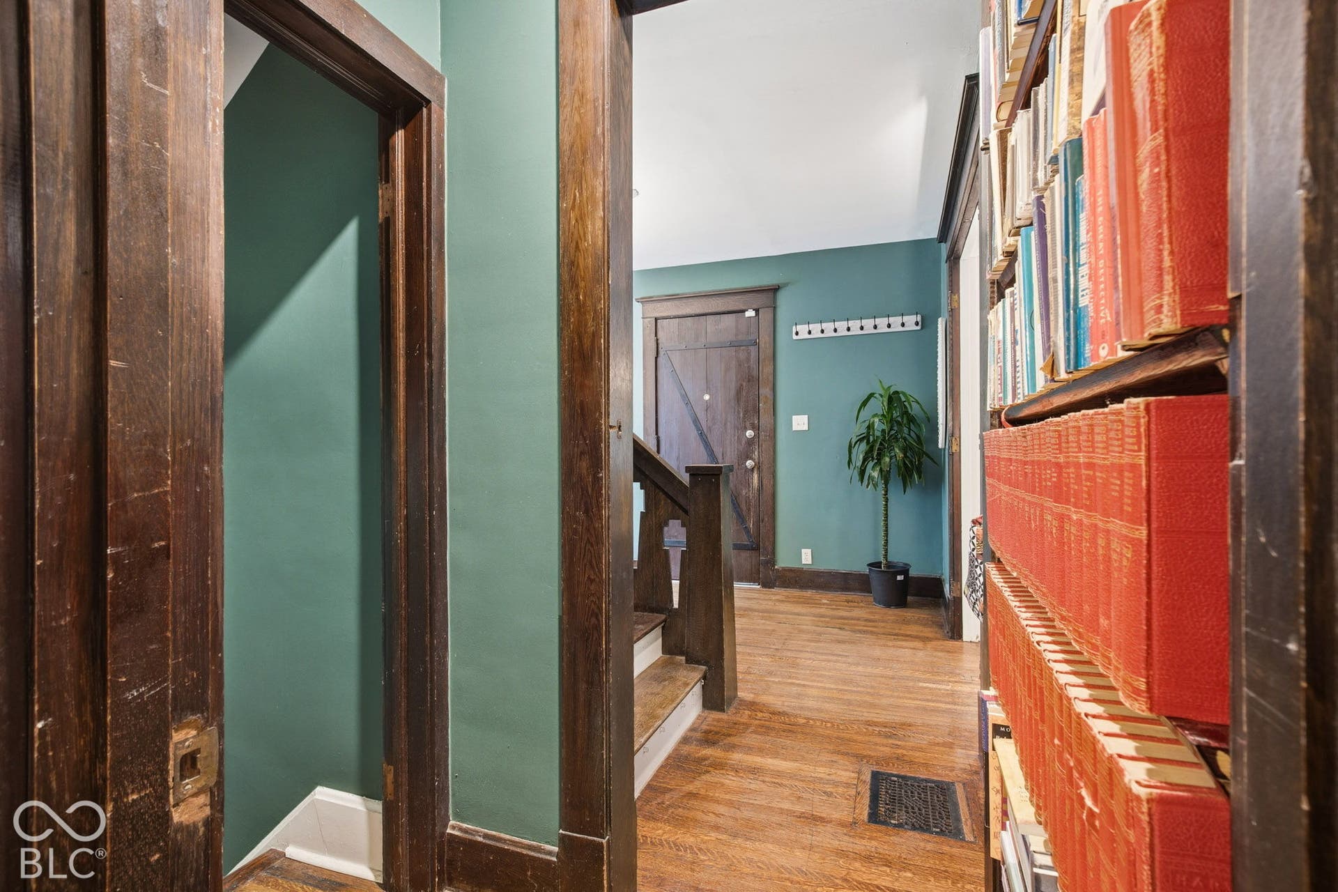 Interior featuring dark-stained wood trim, built-in floor-to-ceiling shelving, wood-finish flooring, and a stained wood staircase with detailed newel post