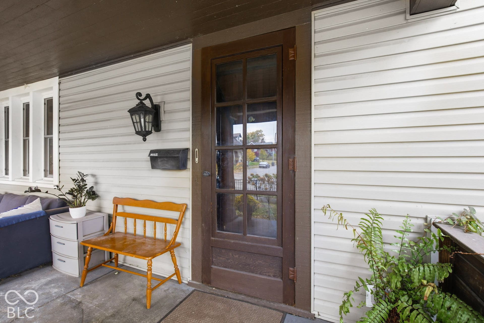 Covered front porch with horizontal siding, glass-paneled wooden storm door, and decorative wall-mounted exterior lighting