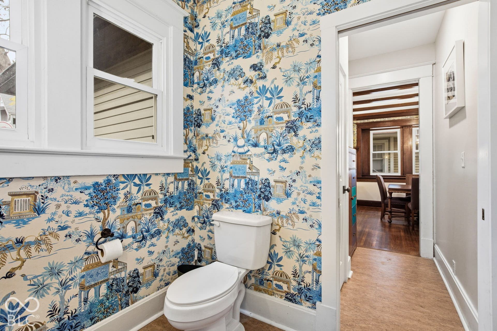 Bathroom featuring decorative patterned wallpaper, a white porcelain toilet, wood-finish flooring, and crisp white window and door casing
