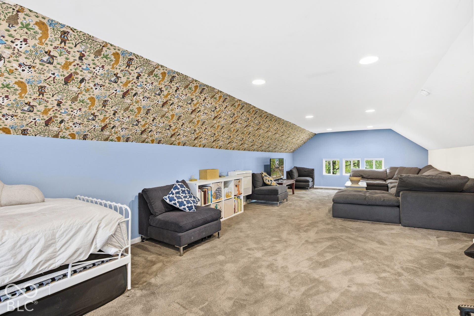 Expansive room featuring vaulted ceilings, recessed lighting, patterned wallcovering on the angled wall, and carpeting