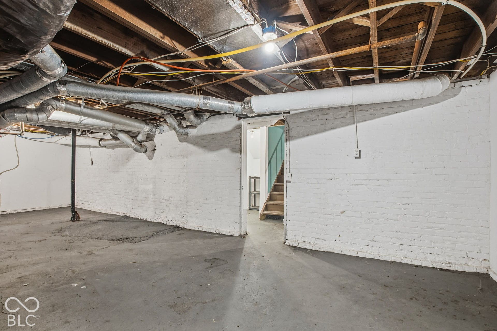 Unfinished basement area featuring painted masonry walls, concrete flooring, exposed ceiling joists, and metal structural support columns