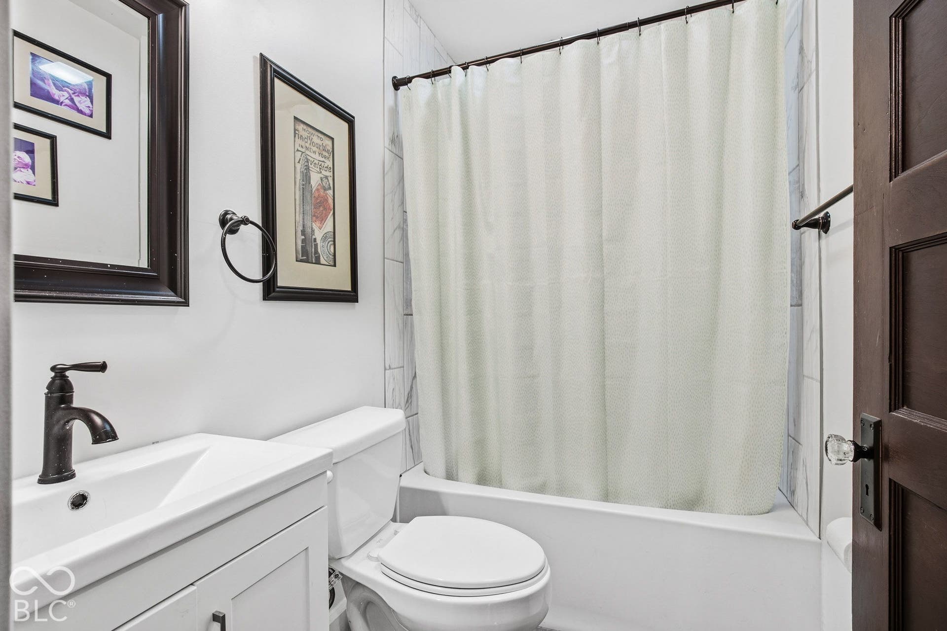 Bathroom featuring a white vanity with integrated basin, oil-rubbed bronze faucet, wall-mounted towel ring, and a porcelain-finish tub with tile surround