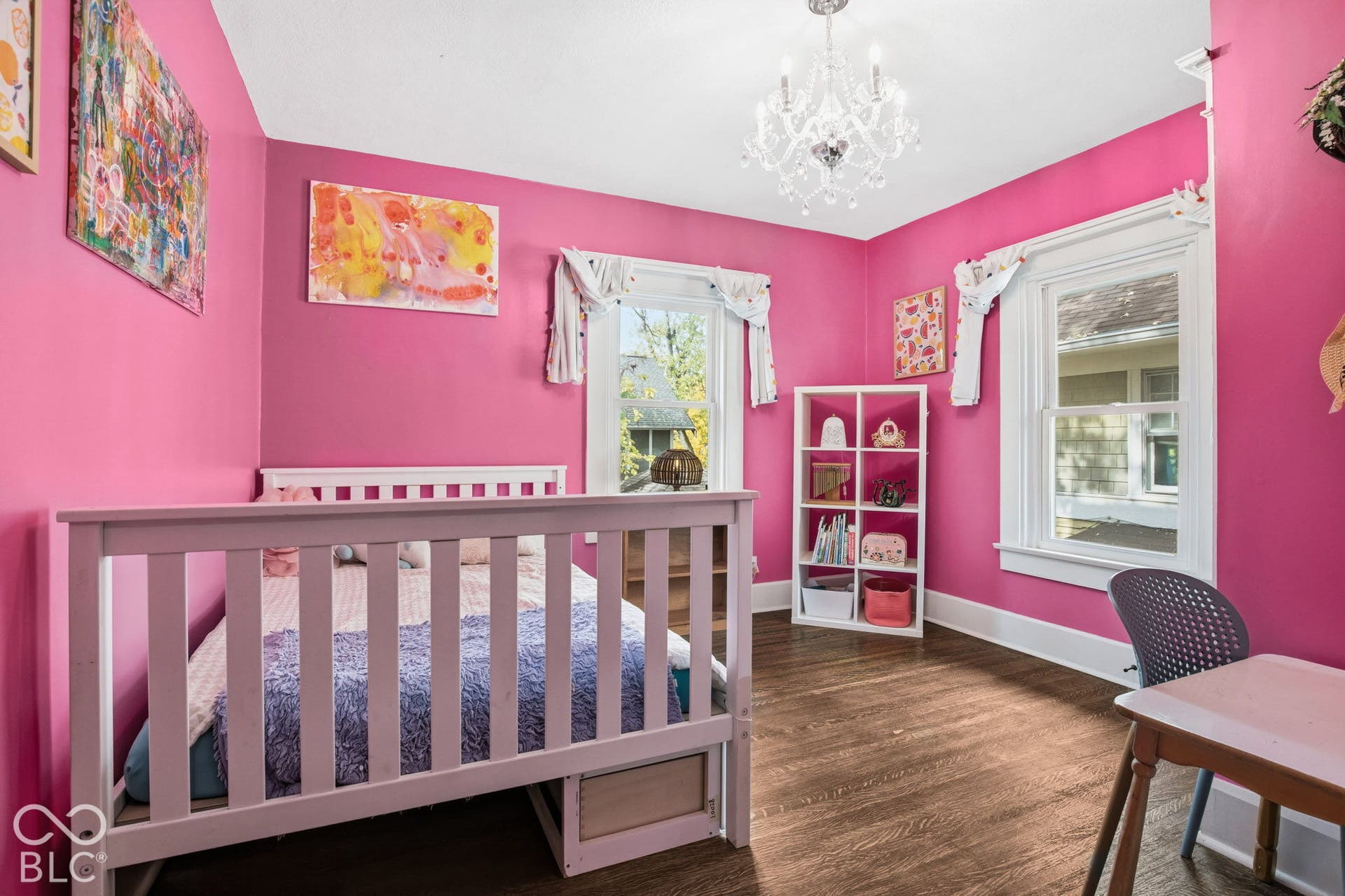 Room featuring wood-finish flooring, two windows with white trim, and a decorative multi-arm chandelier
