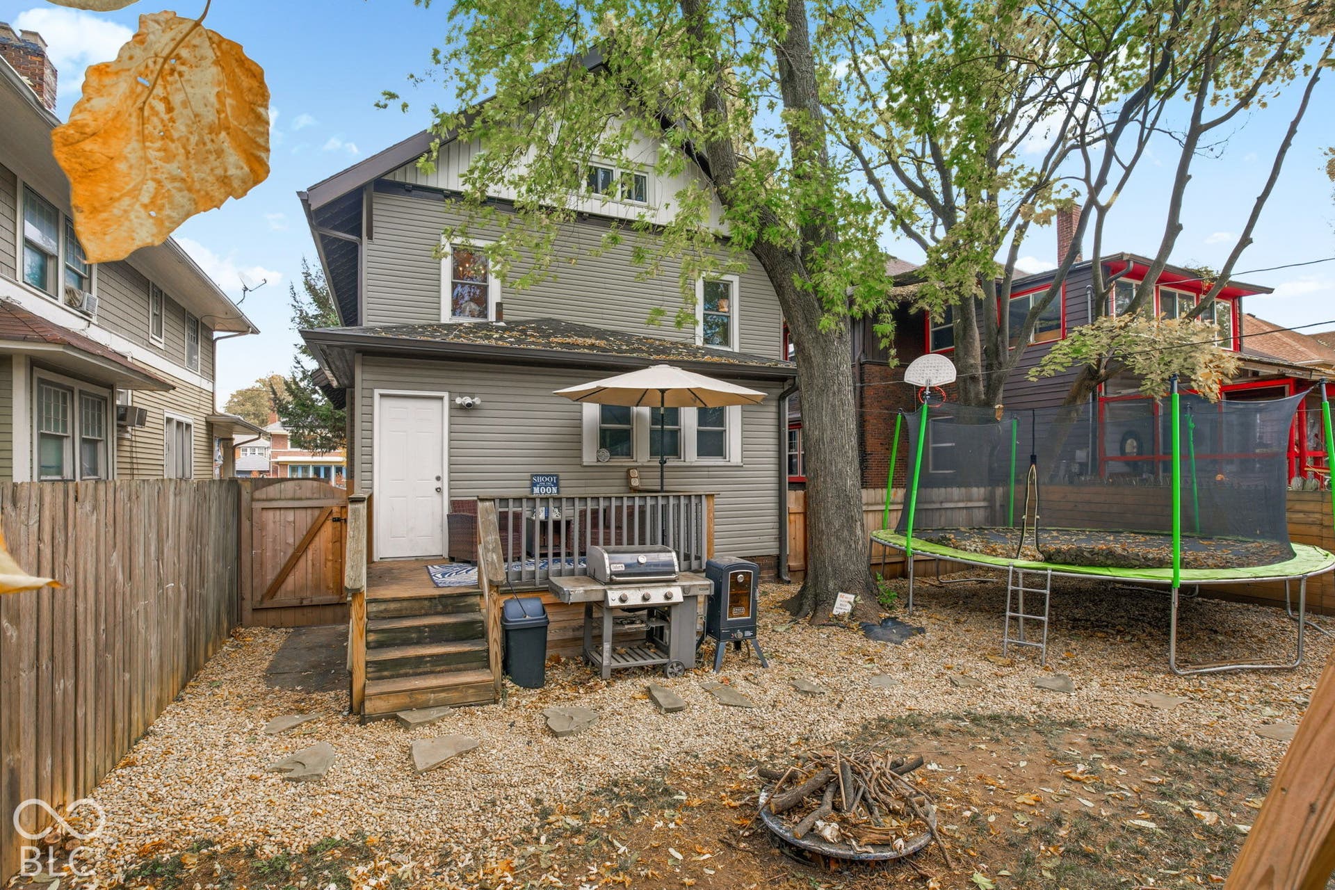 Backyard featuring a raised wooden deck, horizontal siding exterior, mature tree, privacy fencing, and stone-accented ground covering