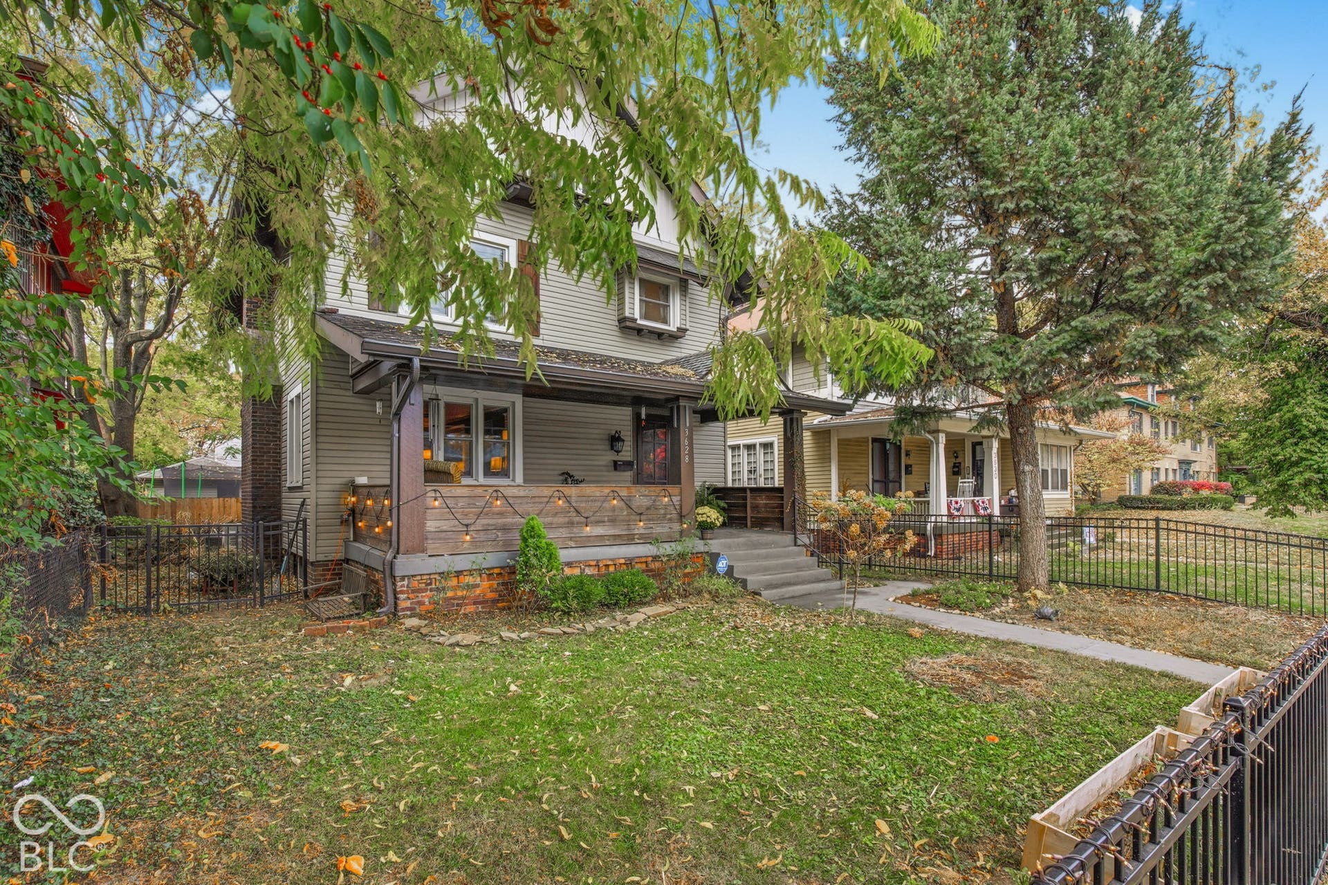 Two-story residence featuring horizontal siding, a covered front porch with wood cladding, brick foundation detailing, and black metal perimeter fencing