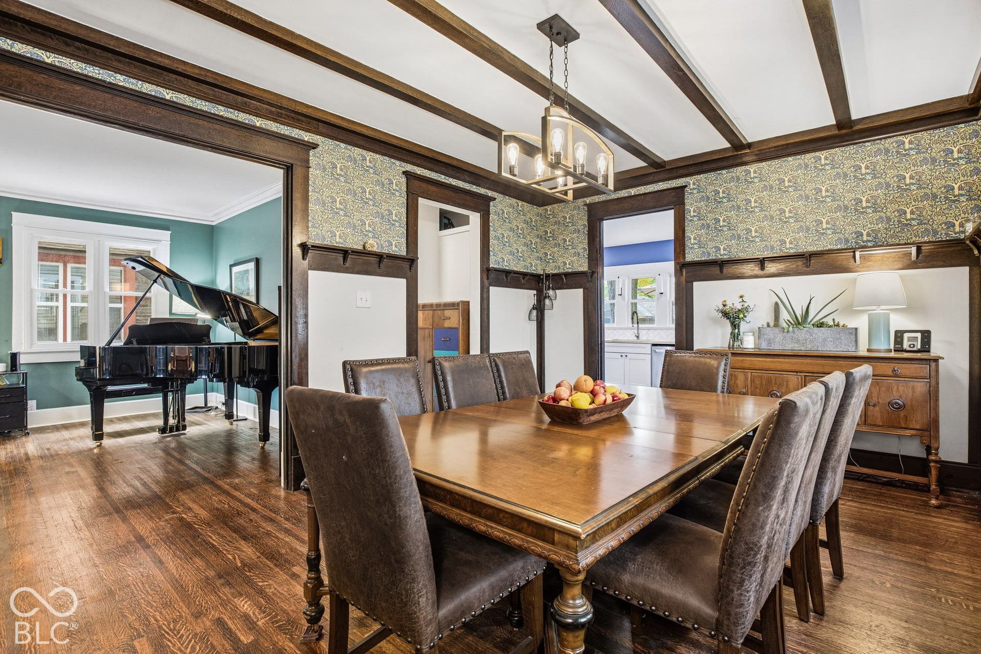 Dining area featuring wood-finish flooring, exposed ceiling beams, decorative wall wainscoting, and a multi-light metal pendant fixture