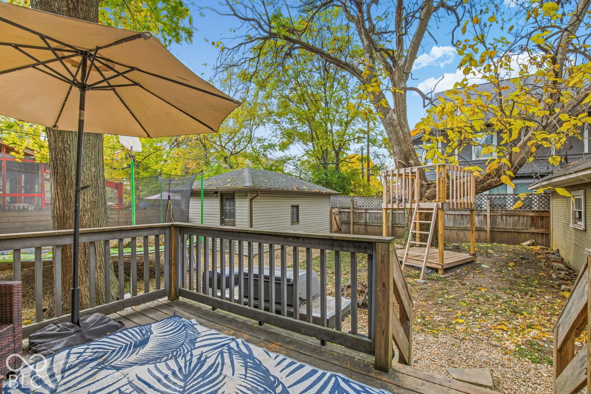 Backyard featuring an elevated wood deck with railing, detached structure, and mature trees