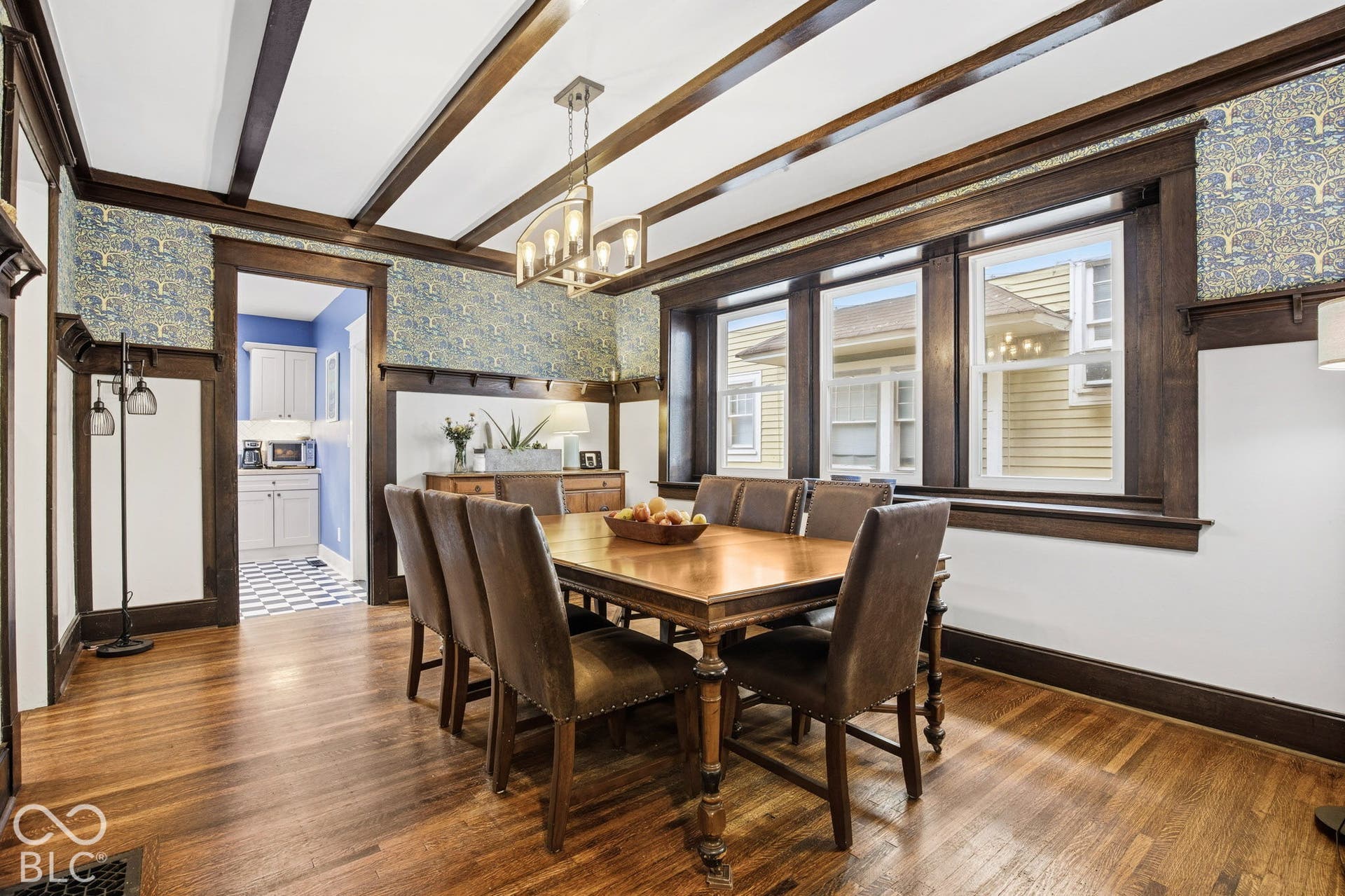 Dining area featuring dark wood-finished ceiling beams, crown molding, extensive window casing, decorative plate rails, and wood-finish flooring