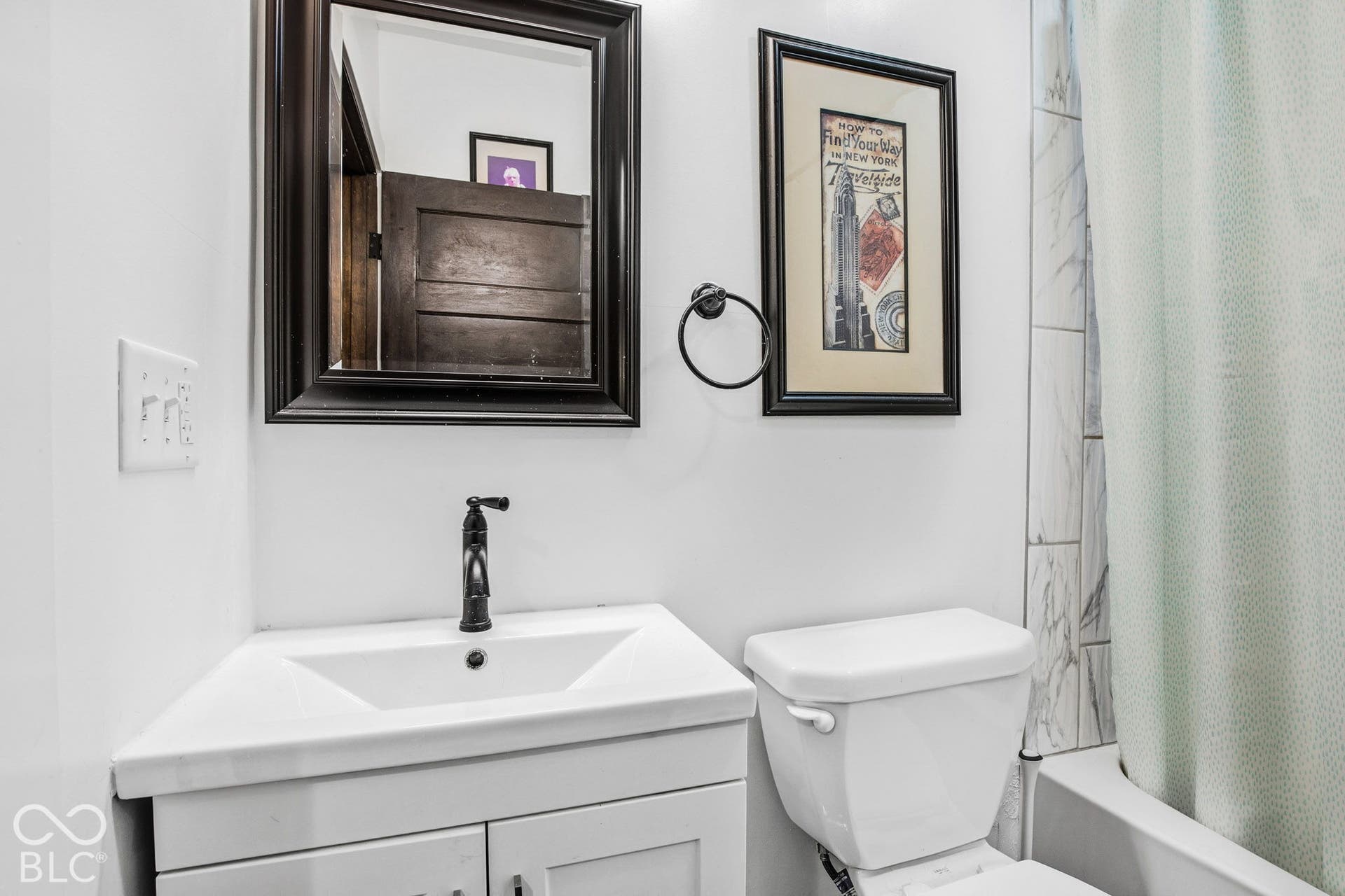 Bathroom featuring a white vanity with an integrated sink, matte black faucet, wall-mounted mirror with a dark frame, and tile shower surround