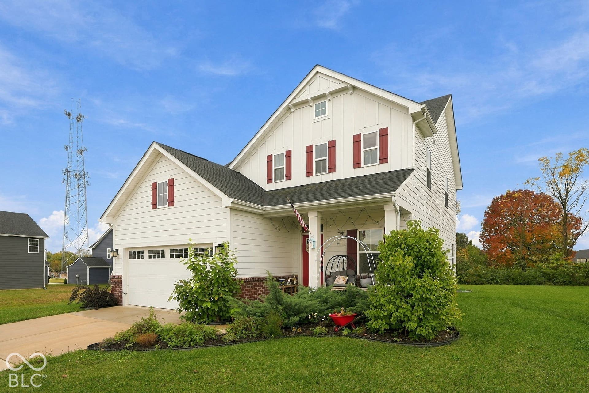 275 Bohicket Road, Whiteland, IN 46184 Two-story residence featuring white horizontal and vertical siding, a covered front porch with square columns, contrasting red window shutters, a two-car garage, and partial brick facade detailing