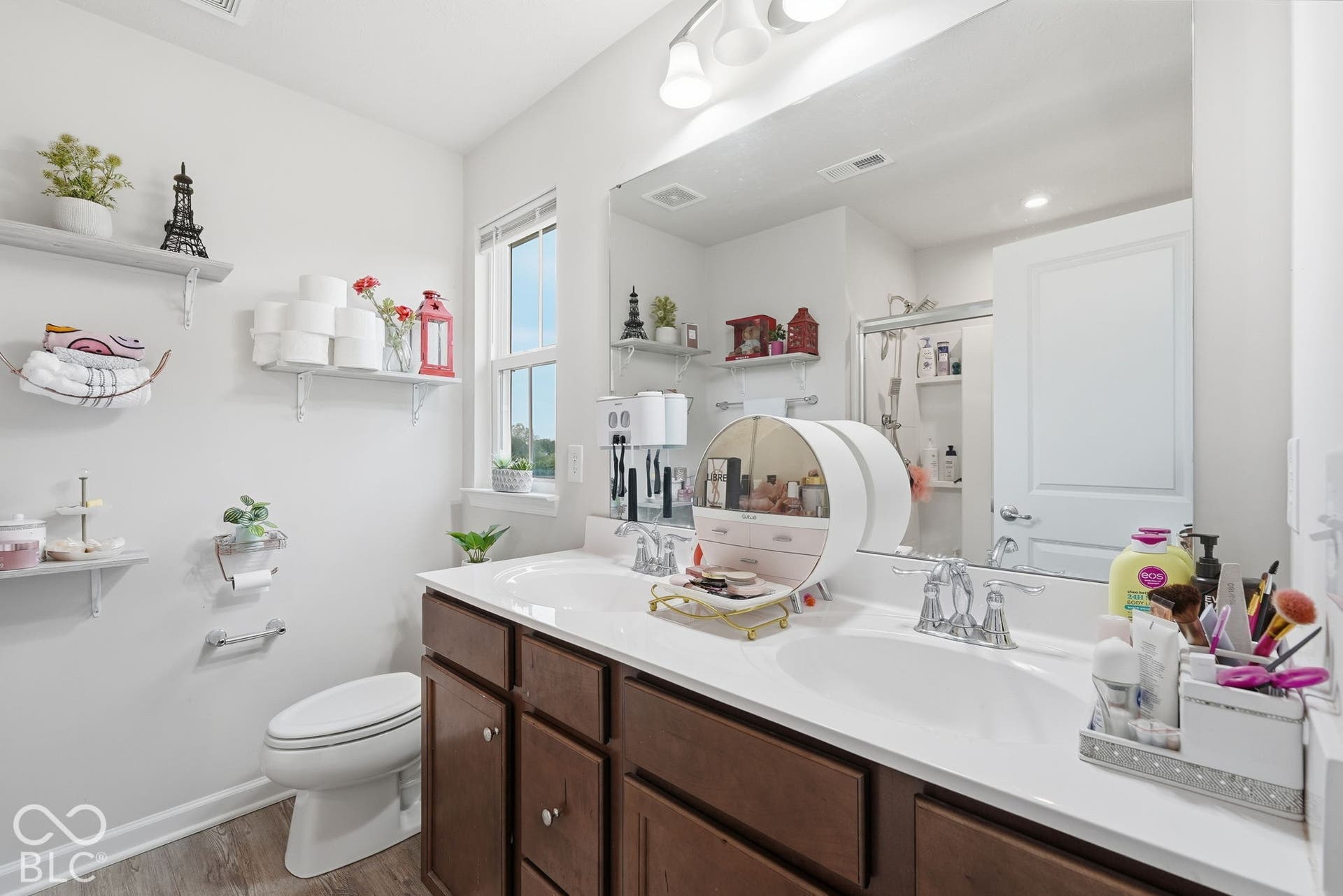 275 Bohicket Road, Whiteland, IN 46184 Double-sink vanity with a solid-surface countertop, wood-finish cabinetry, full-width wall mirror, and wood-finish flooring