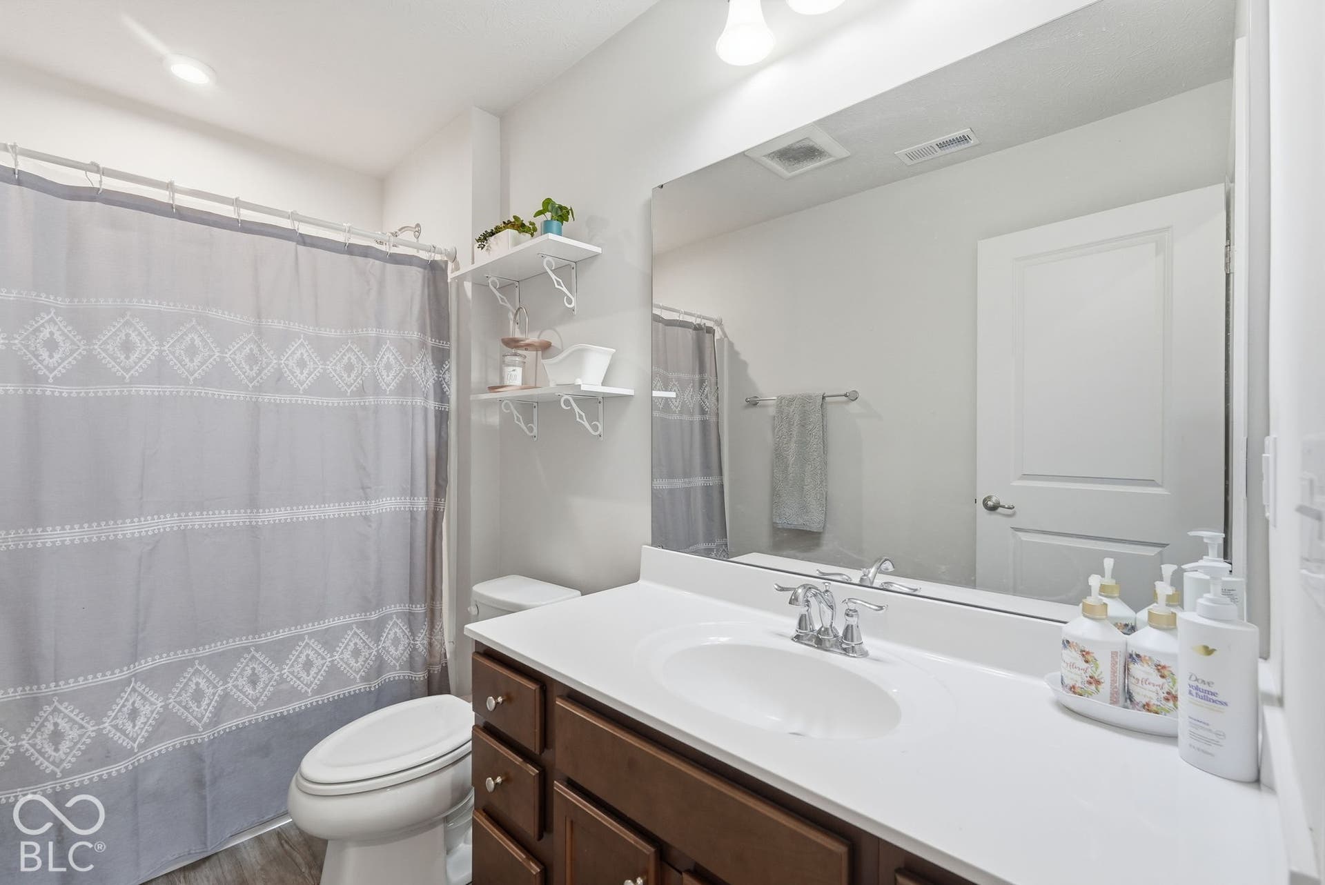 275 Bohicket Road, Whiteland, IN 46184 Bathroom featuring a vanity with wood-finish cabinetry, a white countertop with an integrated oval sink, a wall-to-wall mirror, and wall-mounted shelving