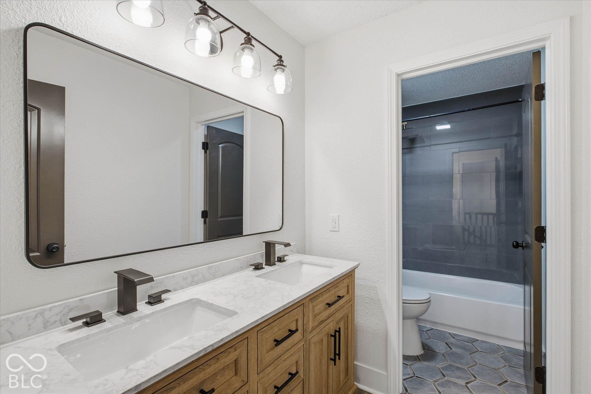 9607 Piper Lake Drive, Indianapolis, IN 46239 Dual-sink vanity with stone-finish countertop, dark metal fixtures, expansive rectangular mirror, and four-light vanity fixture