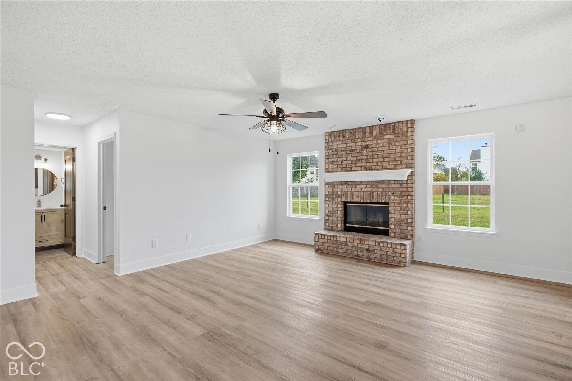 9607 Piper Lake Drive, Indianapolis, IN 46239 Living area featuring wood-finish flooring, floor-to-ceiling brick fireplace with a mantle, and a ceiling fan with integrated lighting