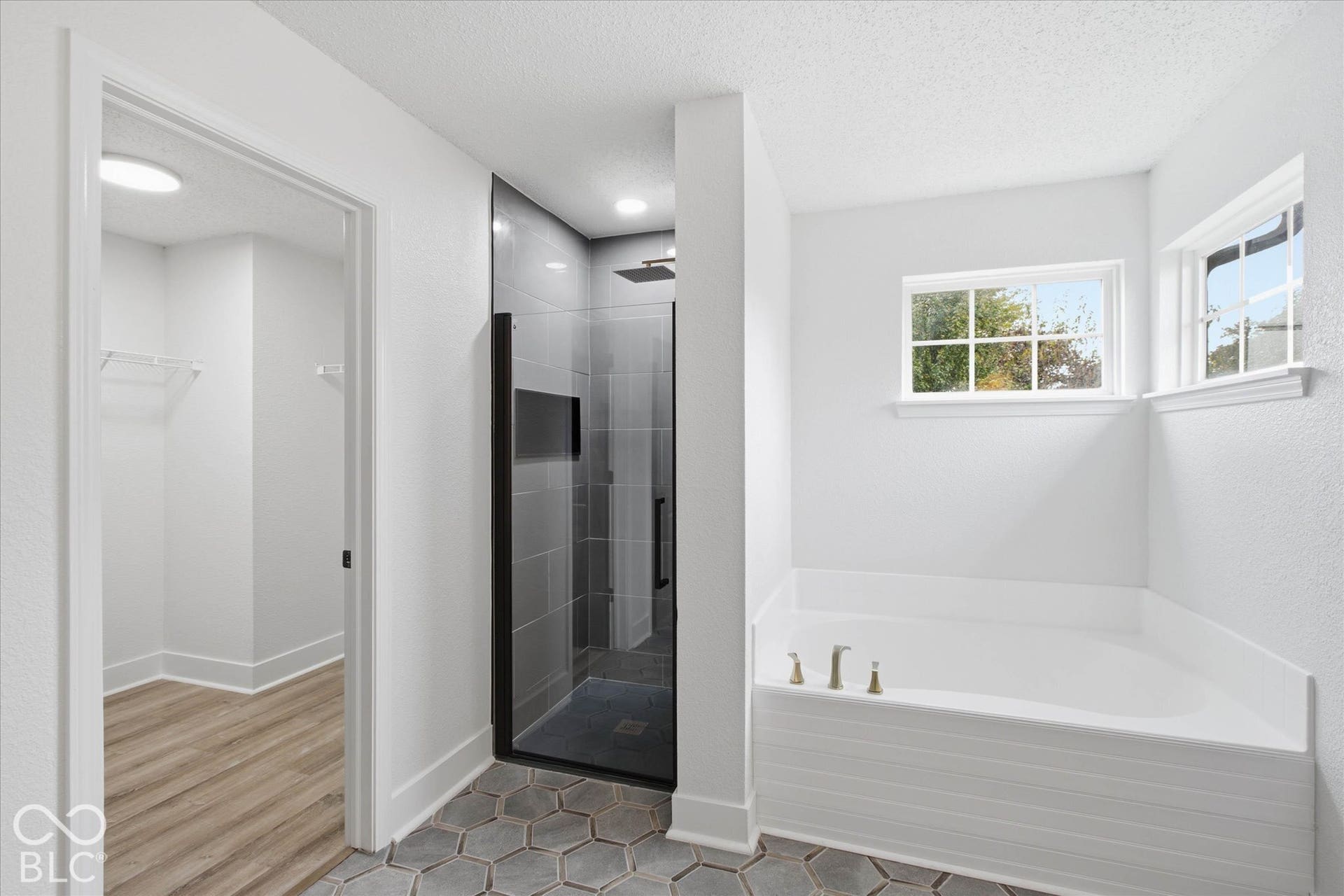9607 Piper Lake Drive, Indianapolis, IN 46239 Bathroom featuring a walk-in shower with floor-to-ceiling tile, frameless glass enclosure, and rainfall showerhead, alongside a built-in soaking tub and hexagonal tile flooring