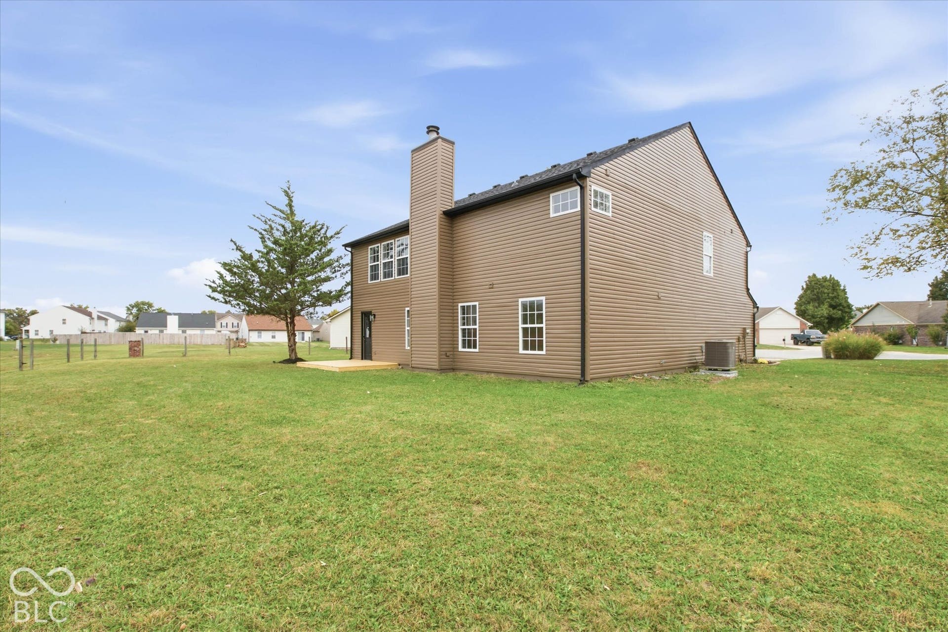 9607 Piper Lake Drive, Indianapolis, IN 46239 Two-story home with brown horizontal siding, an exterior chimney, multiple grid-pattern windows, and an expansive grass yard featuring a wood deck