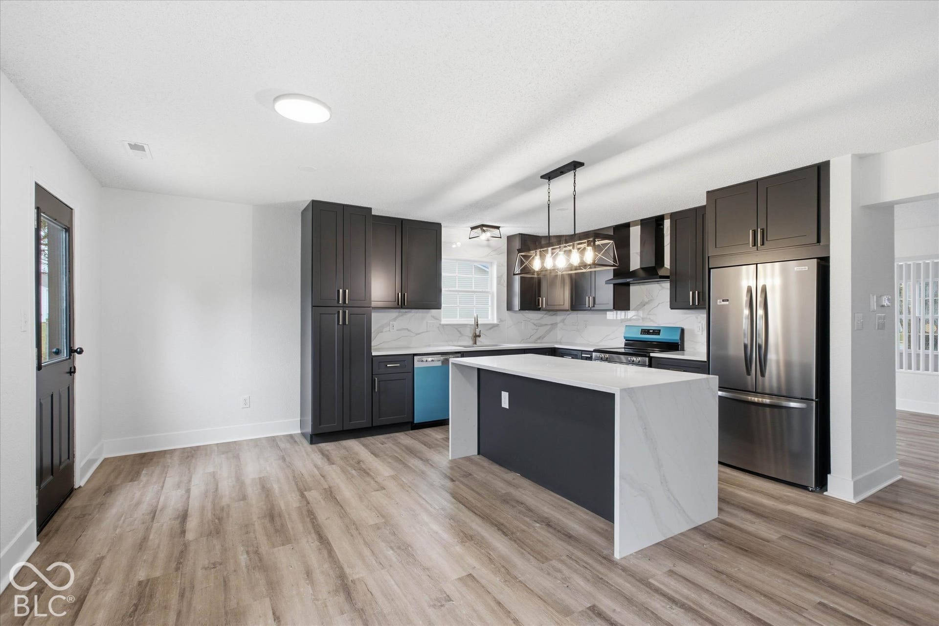 9607 Piper Lake Drive, Indianapolis, IN 46239 Kitchen featuring charcoal cabinetry, waterfall-edge island with light-toned stone-finish countertop, stainless steel appliances, and wood-finish flooring