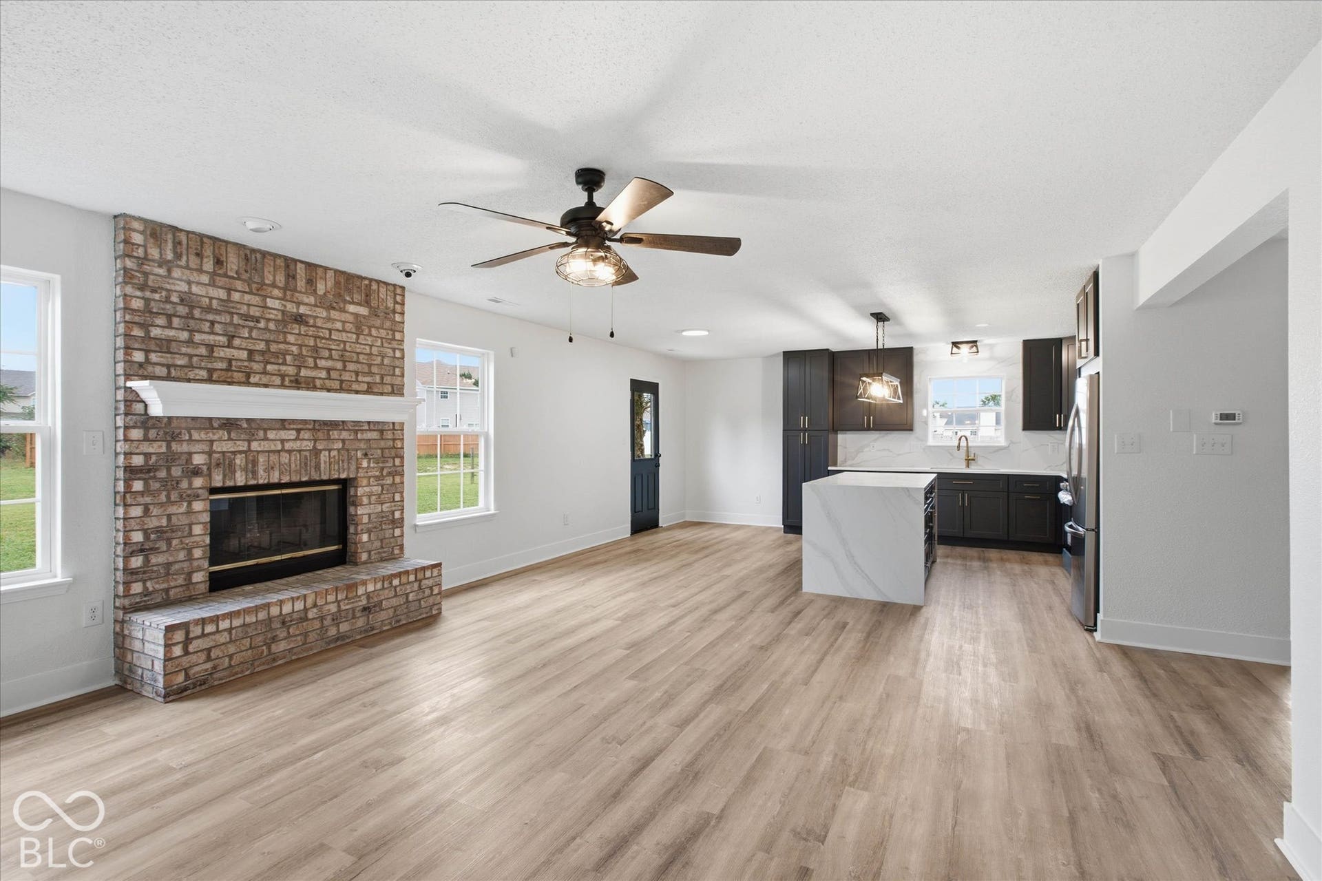 9607 Piper Lake Drive, Indianapolis, IN 46239 Full-height brick fireplace with a wood mantel, wood-finish flooring, kitchen island with a stone-finish waterfall countertop, dark-finish cabinetry, and stainless steel appliances