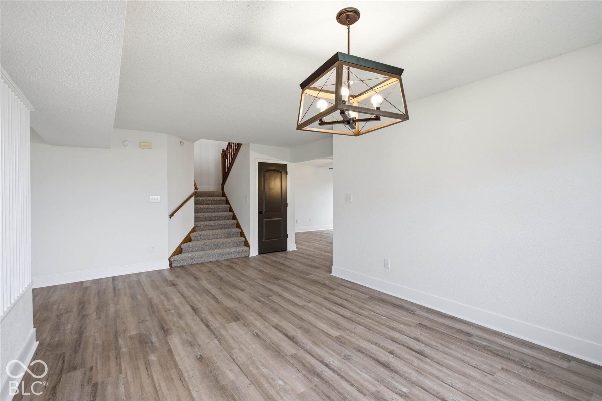 9607 Piper Lake Drive, Indianapolis, IN 46239 Open floor plan featuring wood-finish flooring, a geometric metal chandelier, a carpeted staircase with a wooden handrail, and a raised-panel interior door