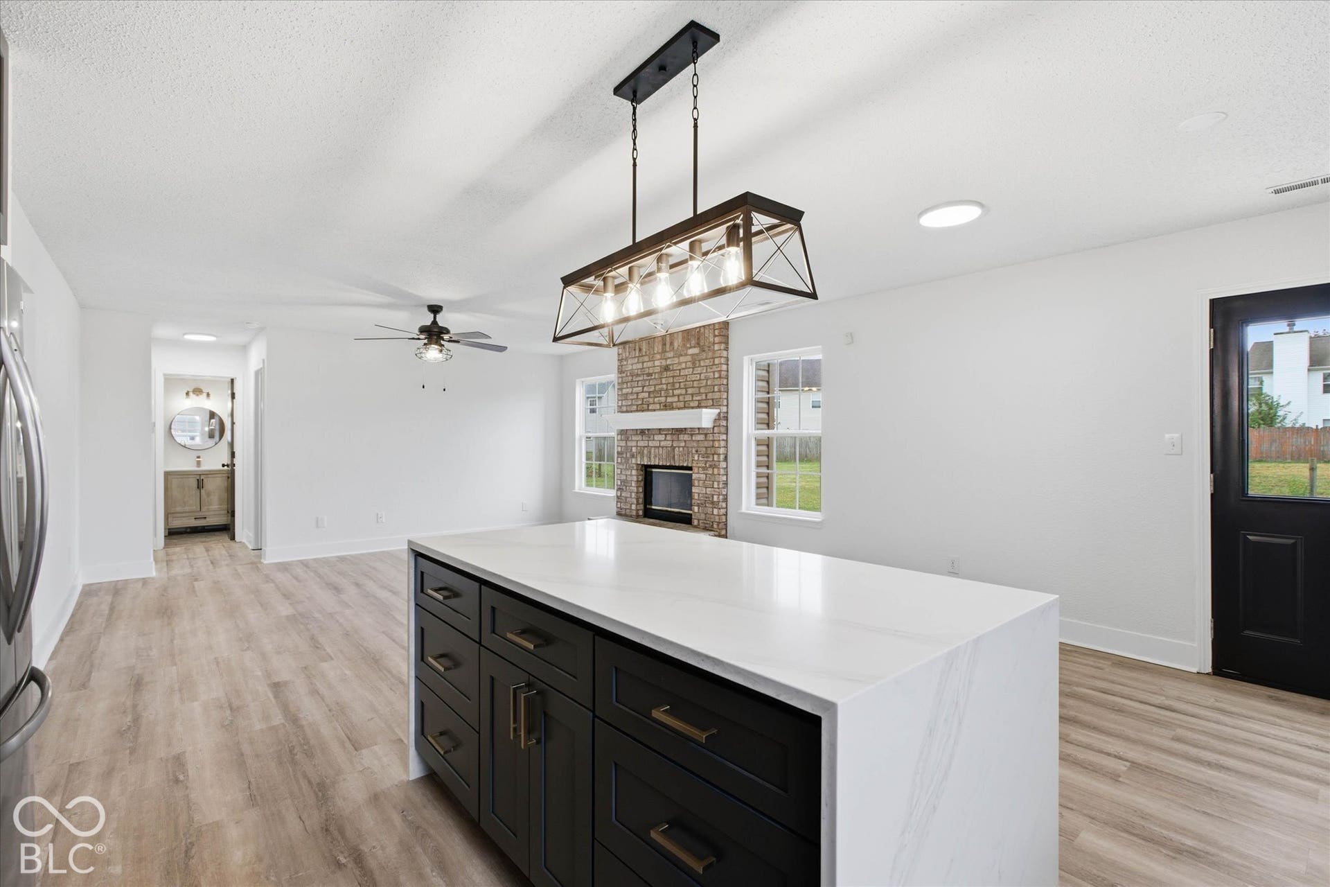 9607 Piper Lake Drive, Indianapolis, IN 46239 Kitchen island with solid-surface countertop and dark-finish cabinetry, wood-finish flooring, brick-accented fireplace, and industrial-style metal chandelier