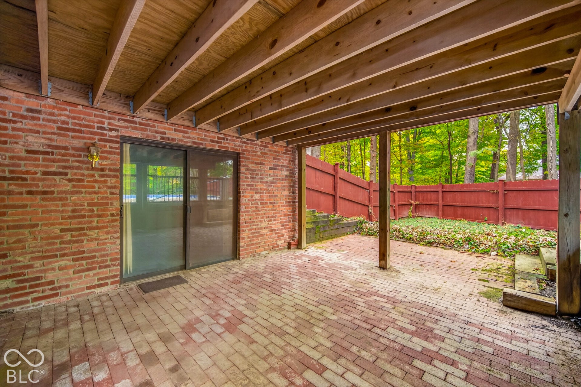Covered brick patio featuring exposed timber ceiling beams, sliding glass doors, and a decorative brick exterior wall