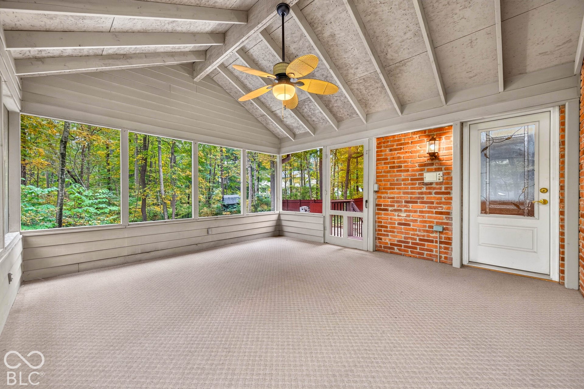 Enclosed sunroom featuring expansive windows, a vaulted beamed ceiling, exposed brick wall, and a ceiling fan