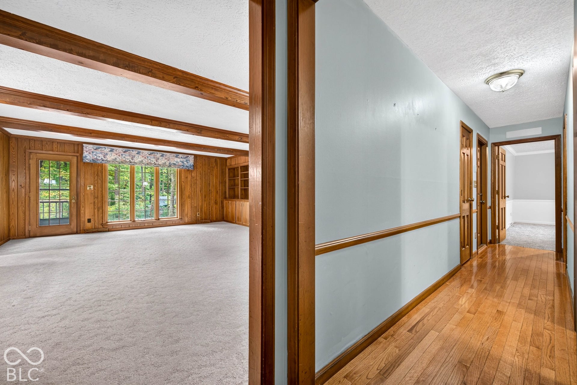 Interior space featuring exposed wood ceiling beams, wood-paneled walls, built-in cabinetry, and hardwood flooring in the hallway