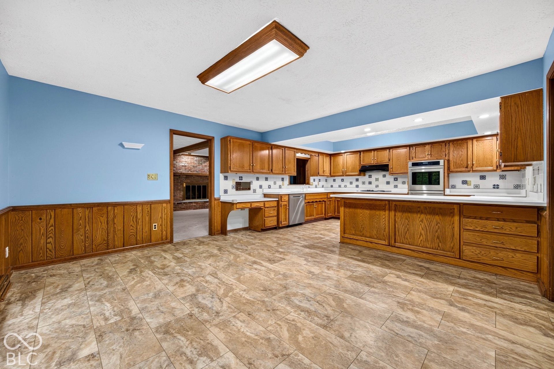 Kitchen featuring wood cabinetry, an integrated peninsula, tile flooring, built-in stainless steel wall oven, and patterned tile backsplash
