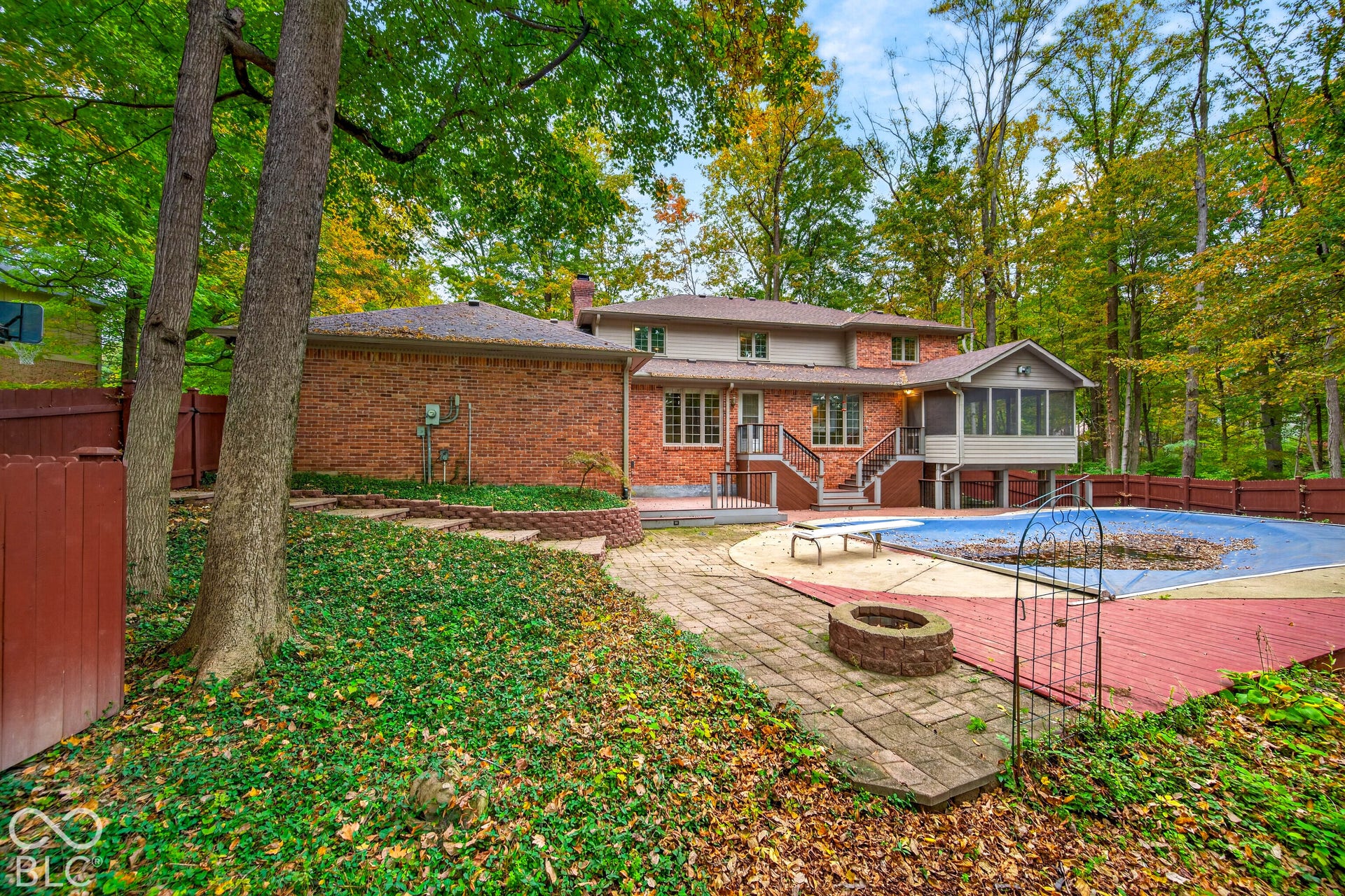 Rear exterior featuring a brick facade, an in-ground swimming pool with surrounding deck, a stone fire pit, and terraced hardscaping