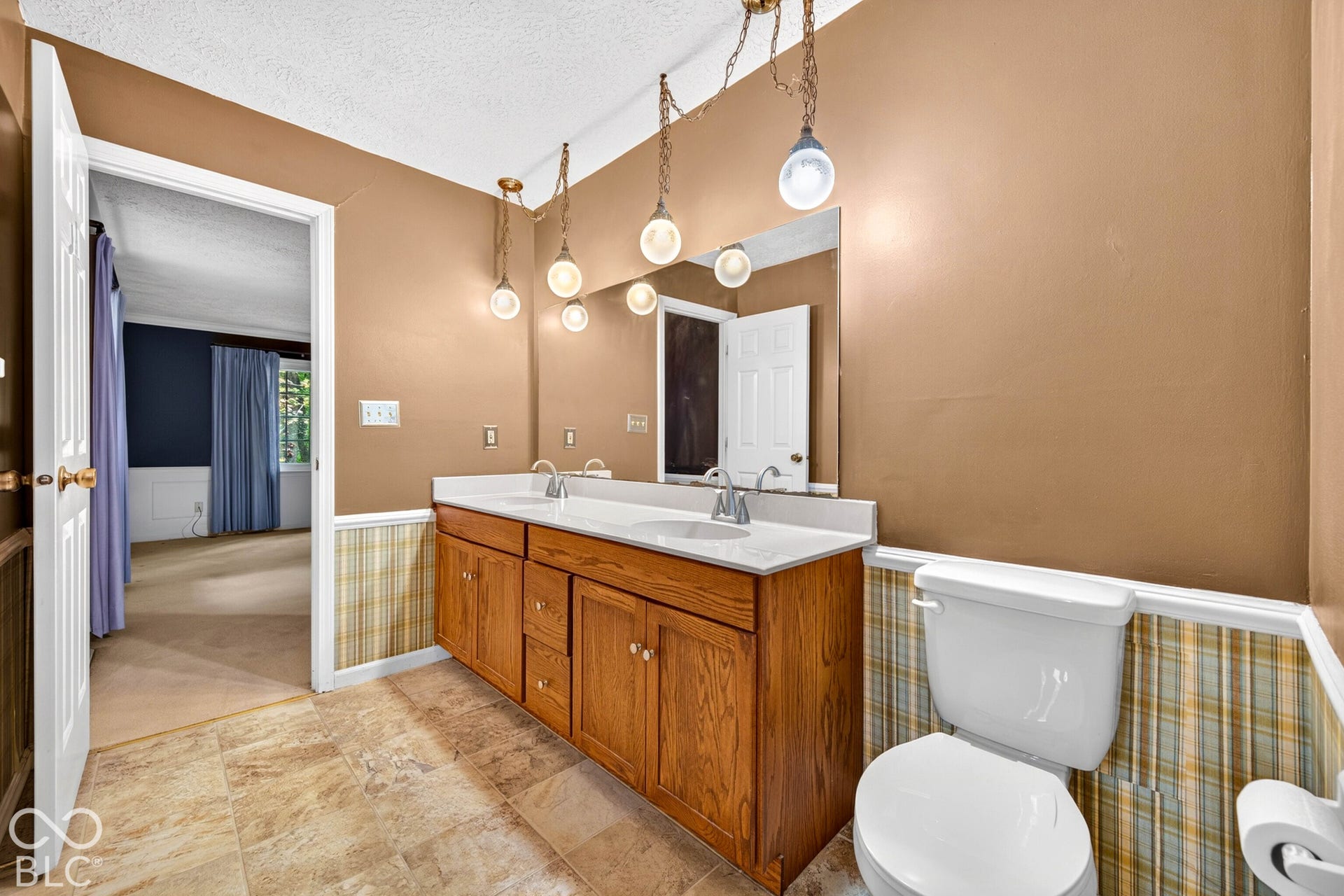Bathroom featuring a dual-sink vanity with wood cabinetry, solid-surface countertop, tile flooring, and multi-pendant lighting