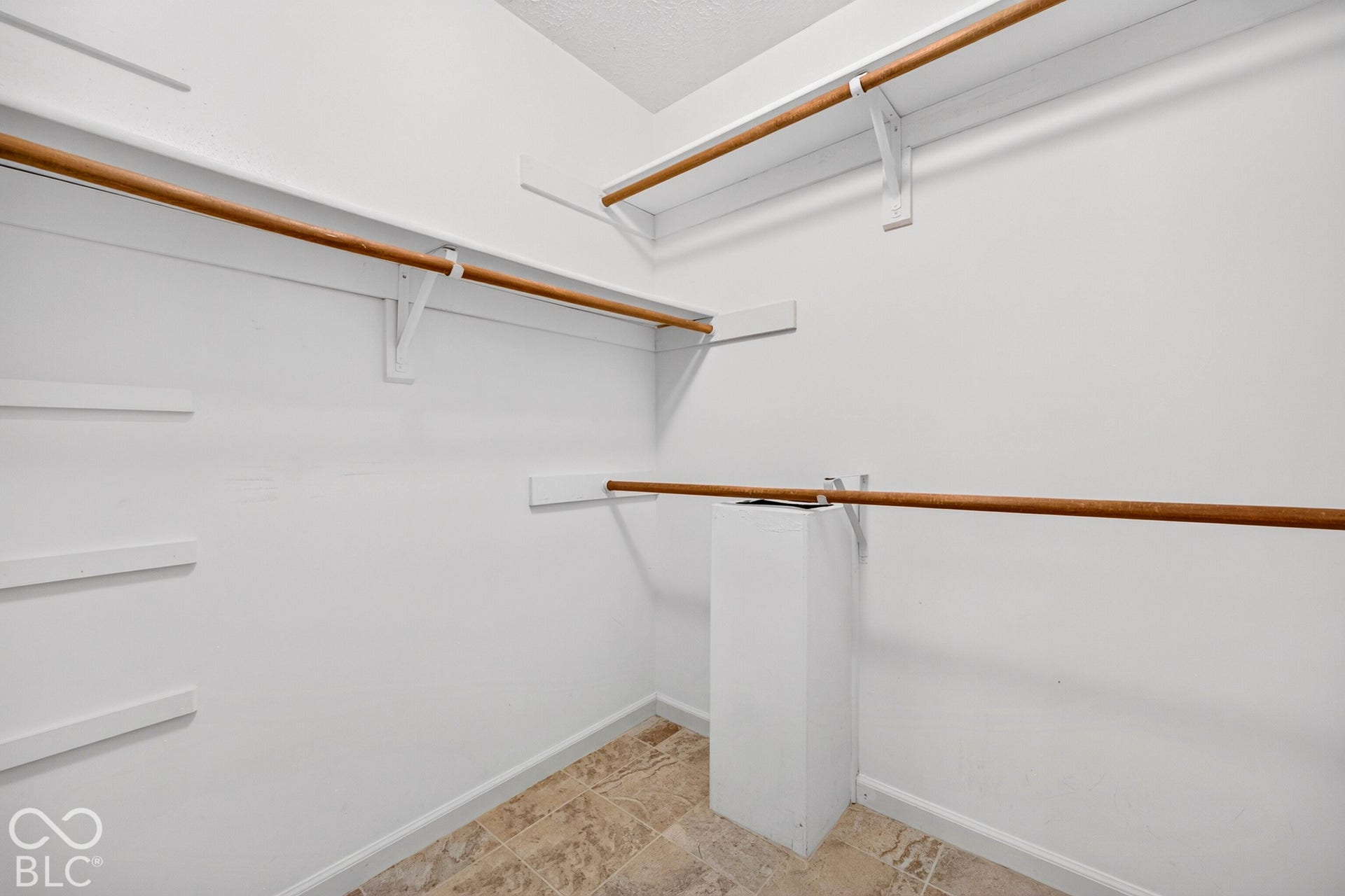 Storage space featuring multi-level wood-tone hanging rods, built-in shelving, and tile flooring