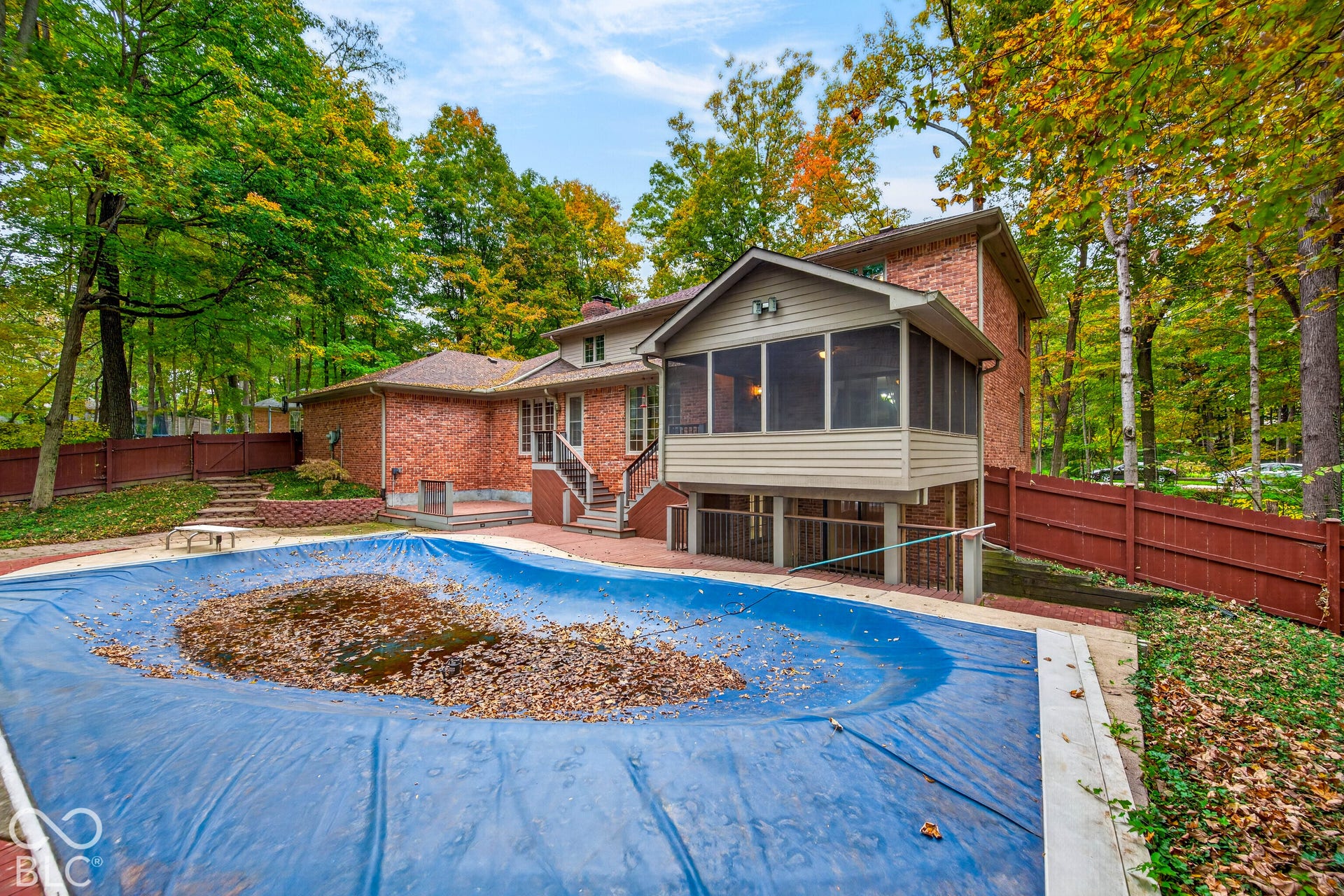 Brick exterior residence featuring an elevated screened porch, in-ground swimming pool with safety cover, paved patio, and perimeter wood fencing