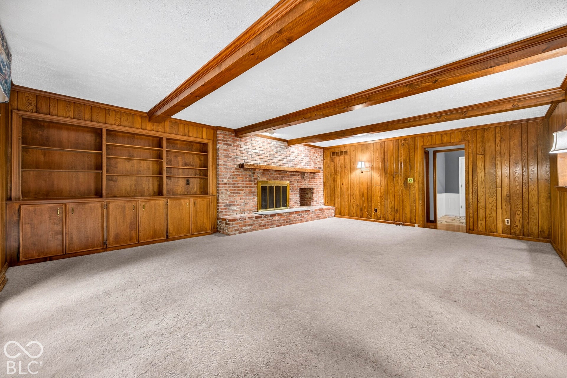Exposed ceiling beams, floor-to-ceiling wood paneling, built-in wooden shelving, and a floor-to-ceiling brick fireplace with a wood mantel