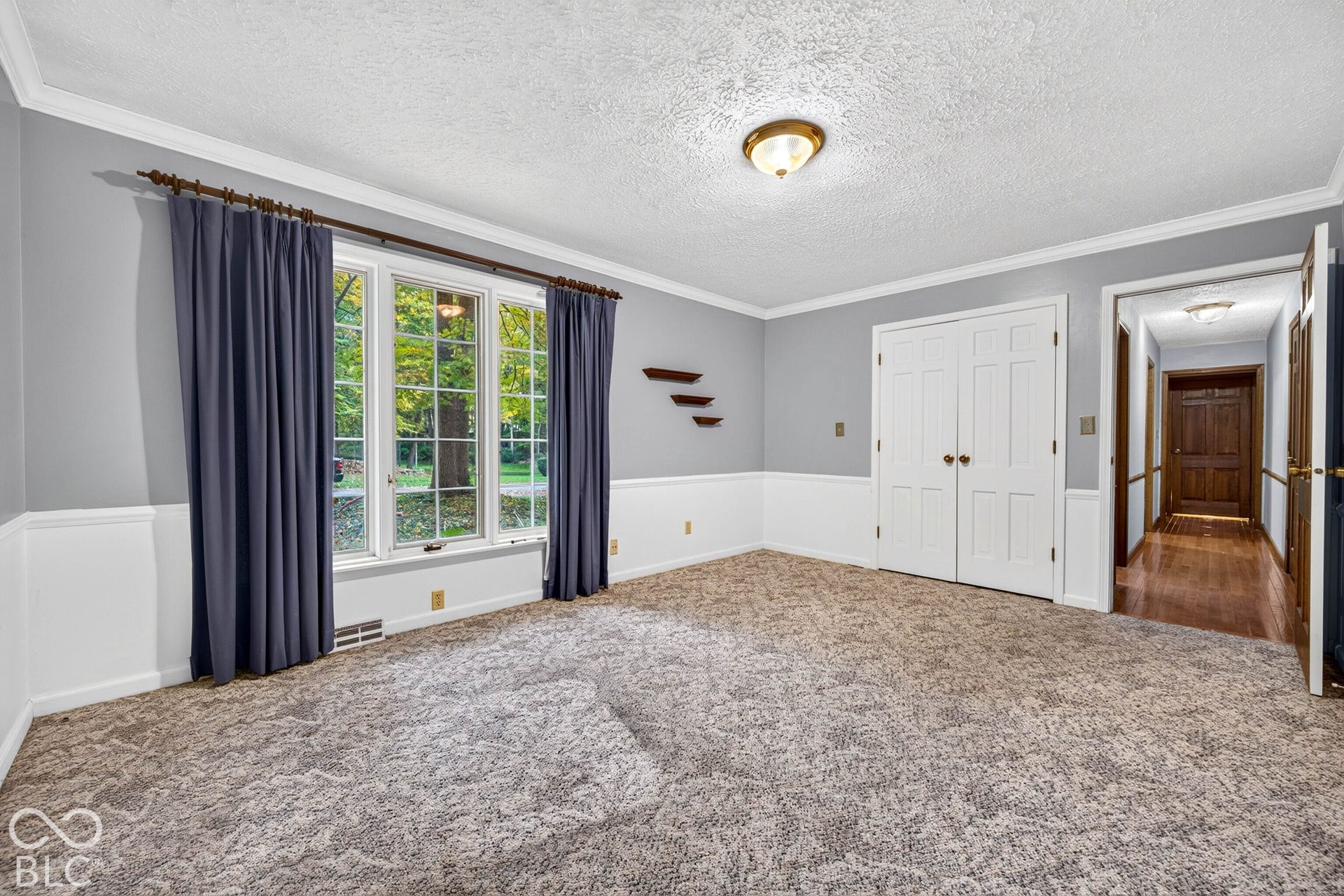 Room featuring triple-pane window configuration, crisp white wainscoting, double-panel doors, crown molding, and wall-mounted shelving
