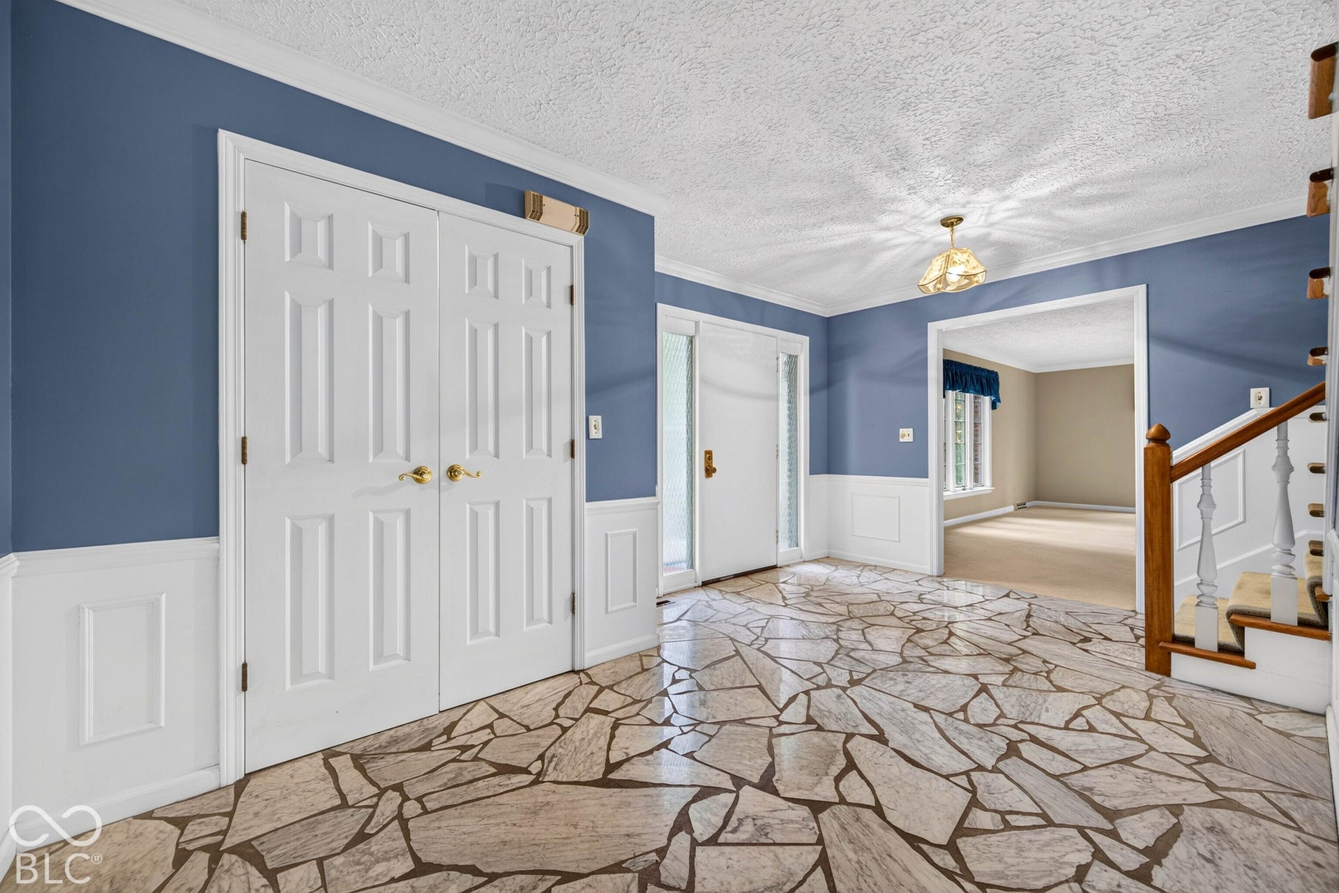 Foyer featuring flagstone flooring, white wainscoting, double-door closet, and staircase with wooden handrail