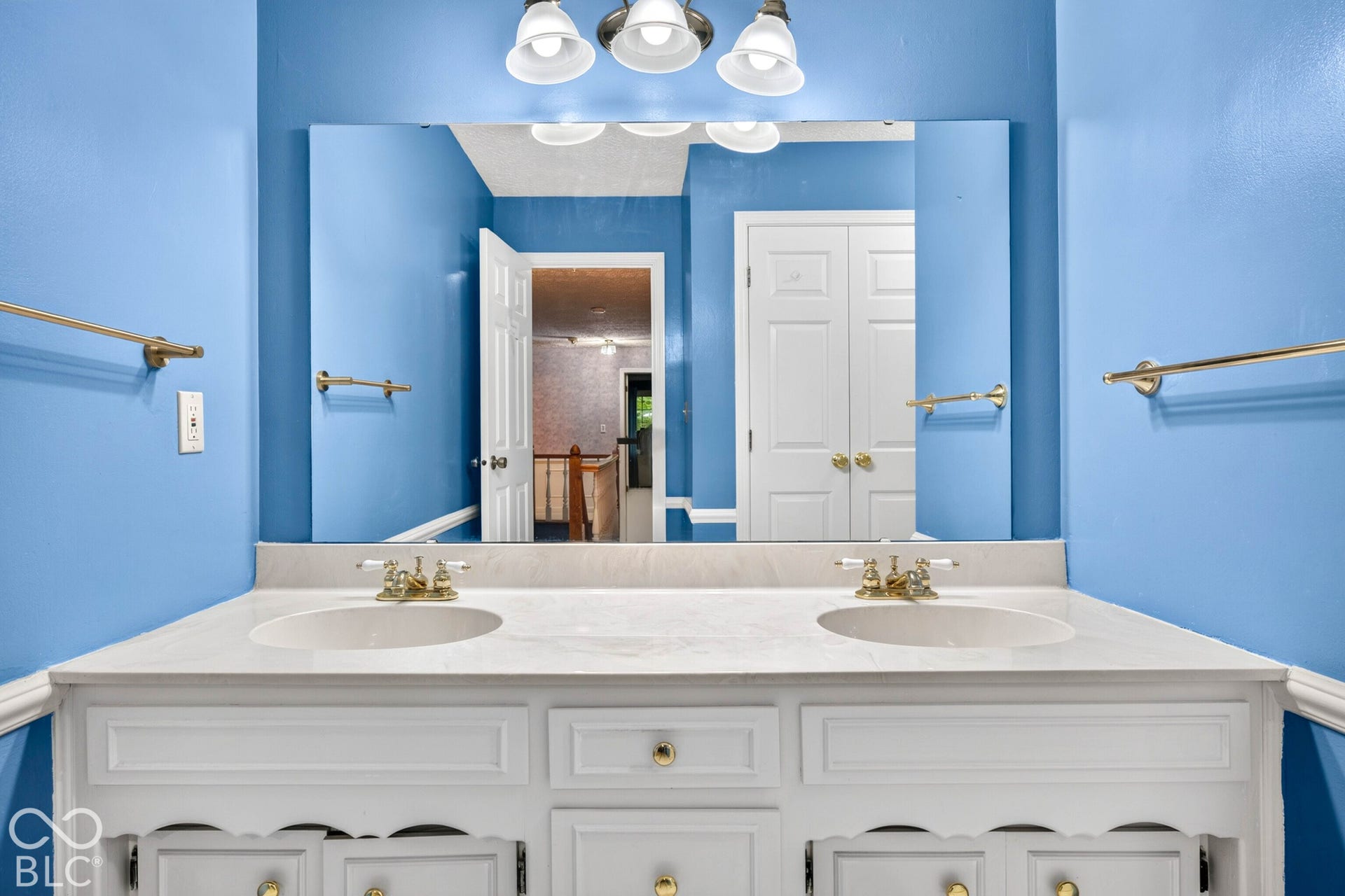Dual-sink vanity with a light-toned countertop, large rectangular wall-mounted mirror, three-light fixture, and metallic hardware