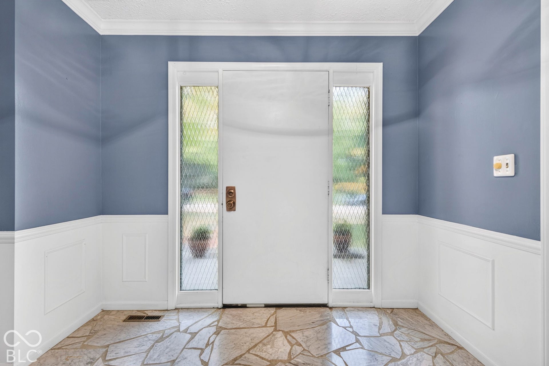 Entryway featuring stone tile flooring, white wainscoting, and a solid door with decorative metal-mesh sidelights