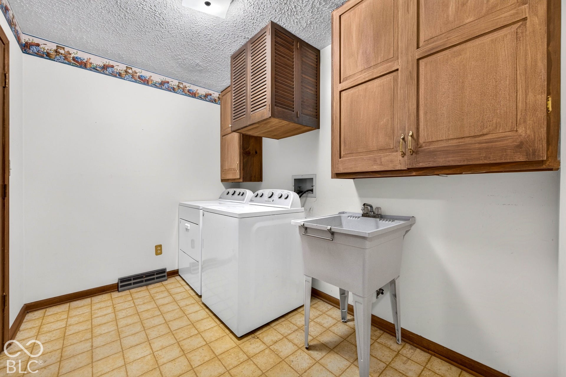 Utility room featuring built-in wooden cabinetry, a wall-mounted louvered storage unit, and a free-standing basin sink